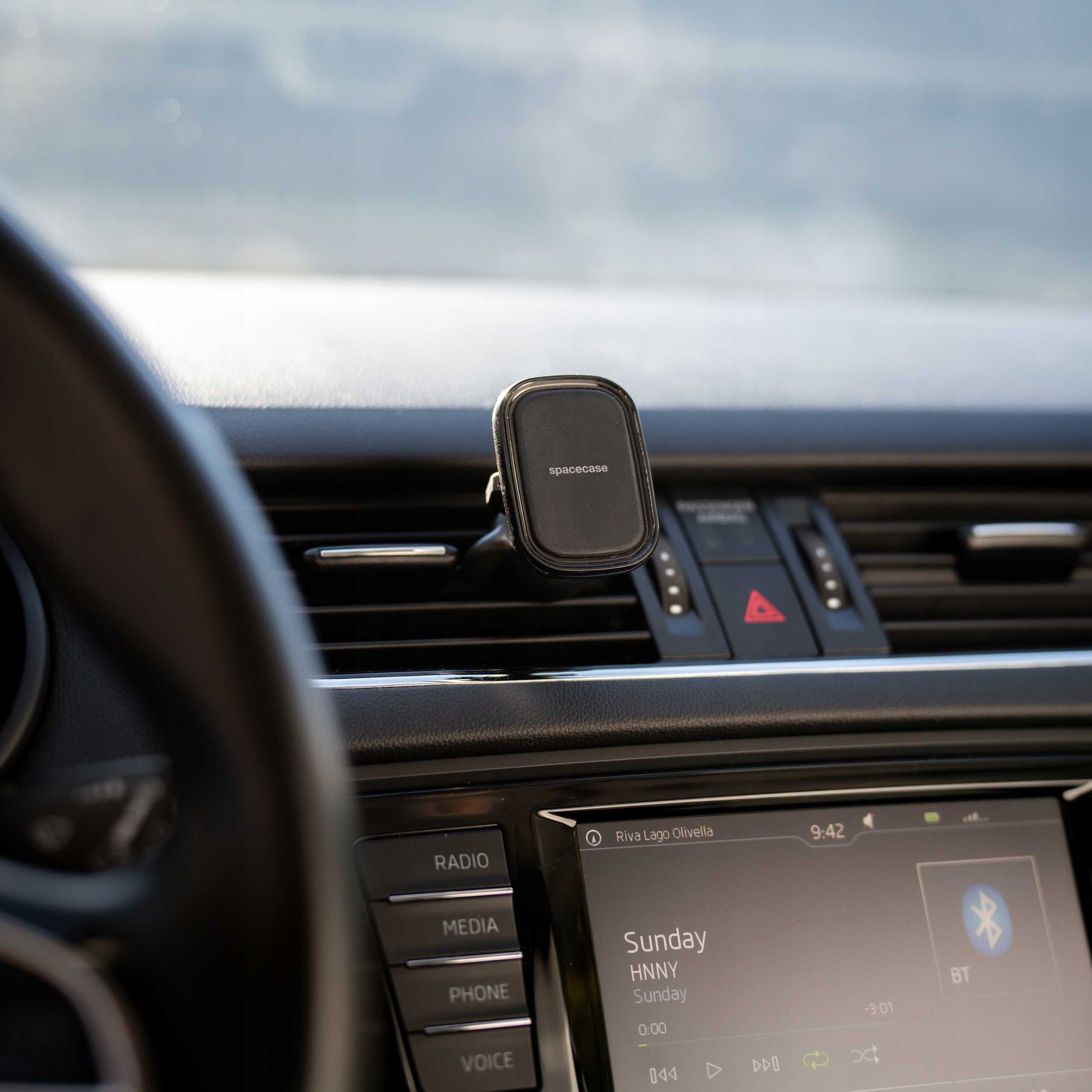 Ujęcie wnętrza samochodu. Uchwyt na telefon z napisem 'spacecase' jest zamontowany na desce rozdzielczej. Widoczne są przyciski radia i multimediów.