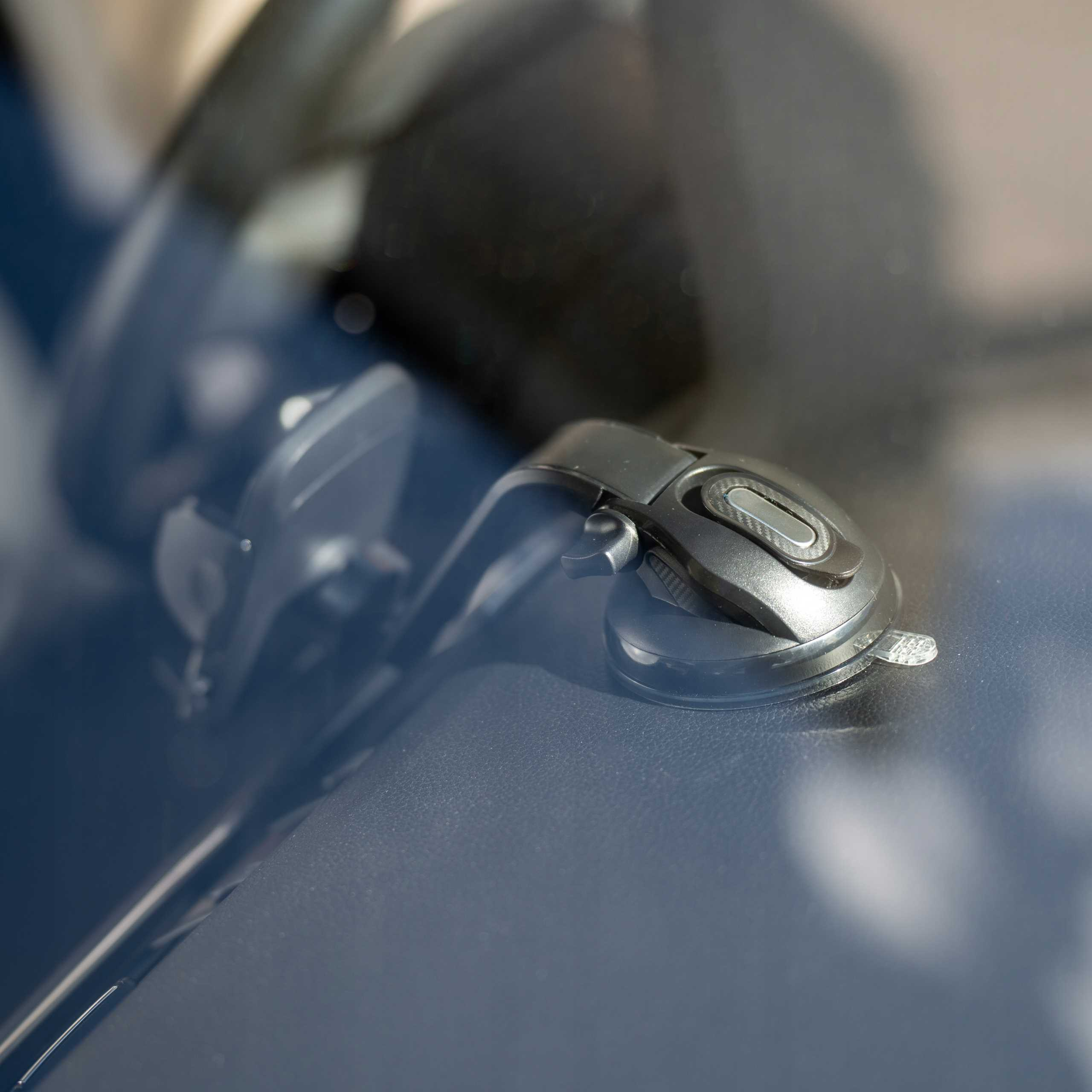 Czarny uchwyt na telefon z przyssawką jest zamontowany na desce rozdzielczej. Widoczna jest przednia szyba i tło.