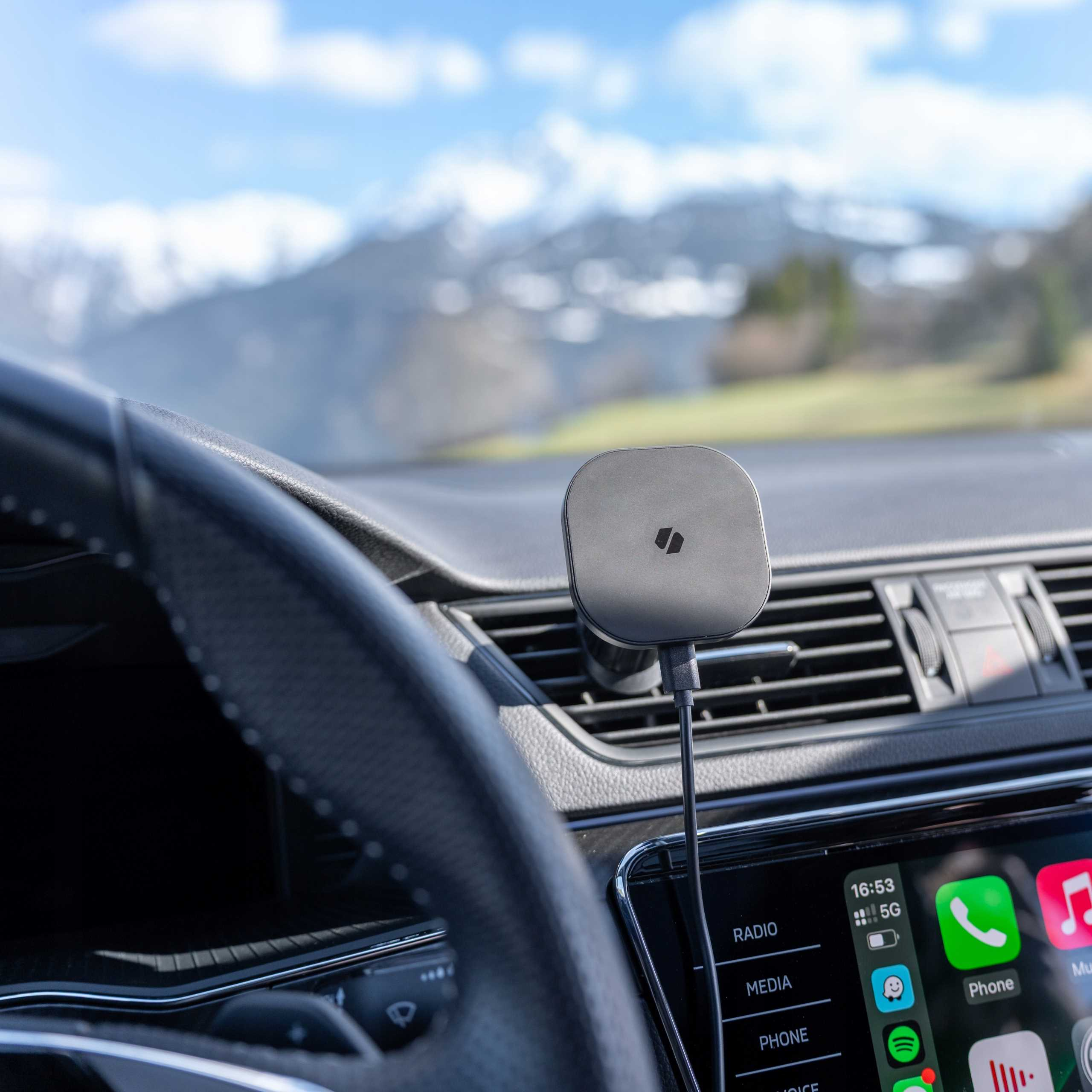 Wnętrze samochodu z uchwytem na telefon. Góry i niebo widoczne przez przednią szybę. Telefon wyświetla aplikacje.
