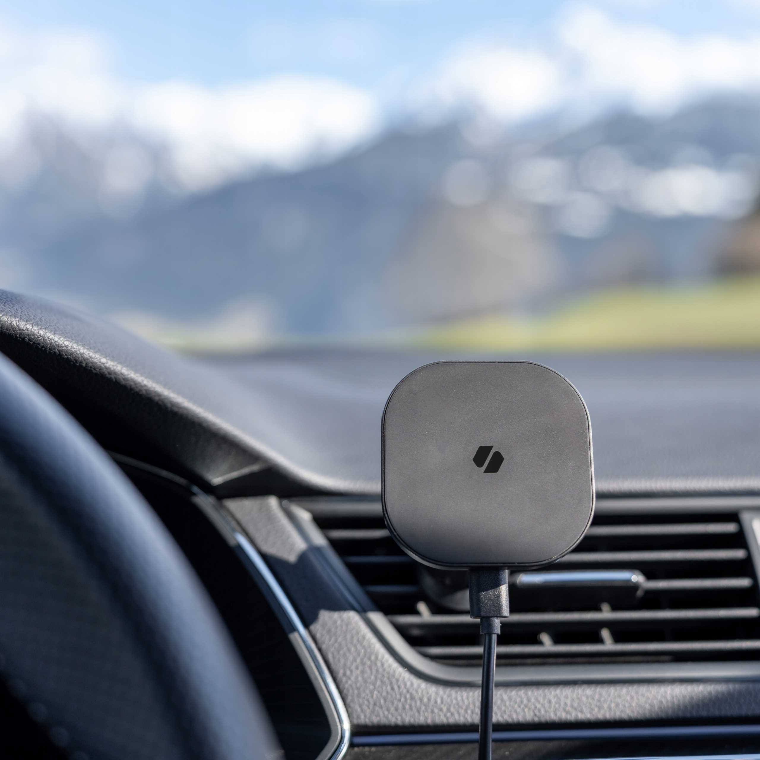 Wnętrze samochodu pokazuje uchwyt na telefon, szczegóły deski rozdzielczej i rozmyty krajobraz górski.