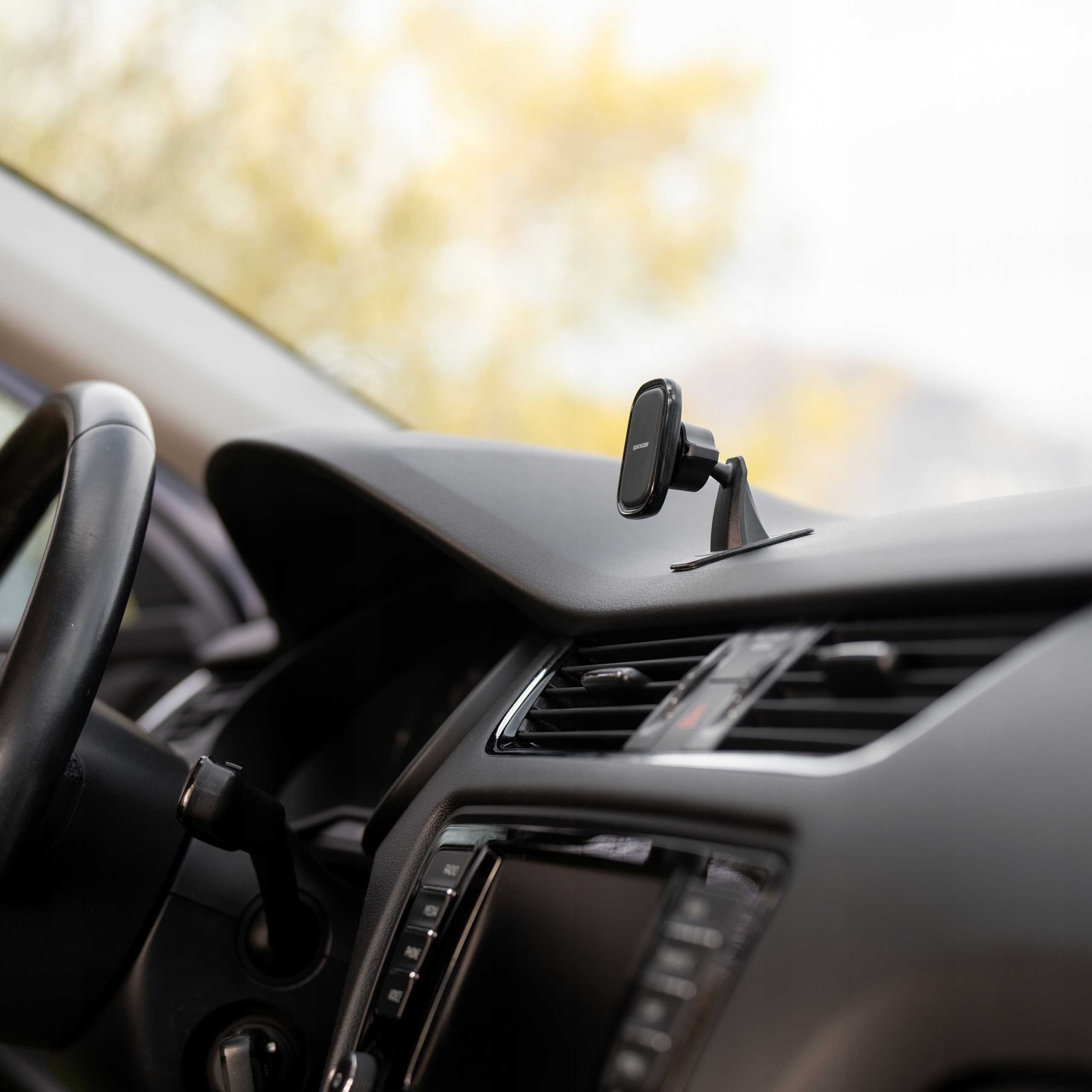 Wnętrze samochodu z czarną deską rozdzielczą, kierownicą i uchwytem na telefon. Tło jest rozmyte.