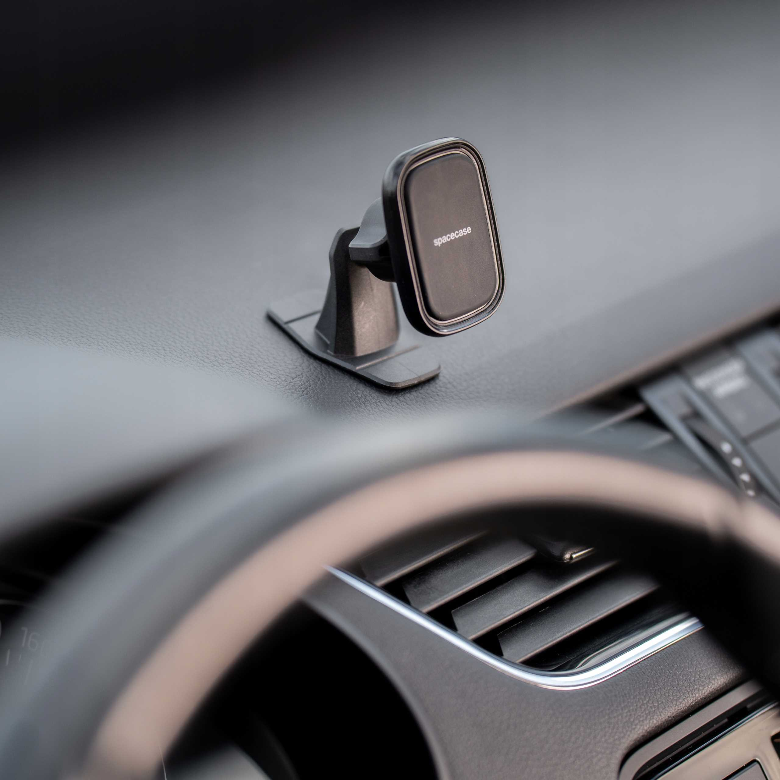 Wnętrze samochodu z uchwytem na telefon na desce rozdzielczej. Kierownica i kratki wentylacyjne widoczne na rozmytym pierwszym planie.