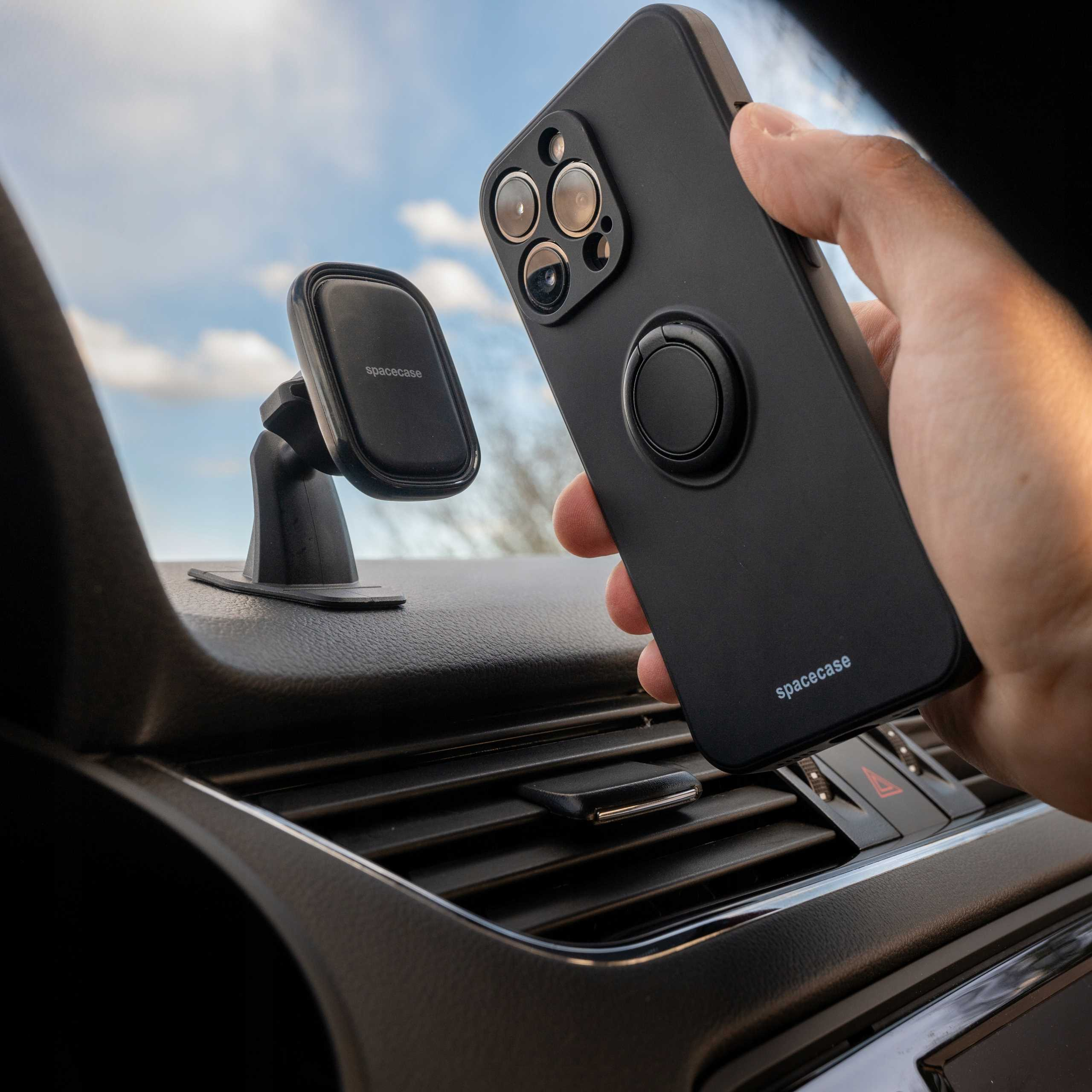 Czarny futerał na telefon z uchwytem na pierścień jest trzymany w pobliżu otworu wentylacyjnego w samochodzie. Widoczny jest również magnetyczny uchwyt do telefonu.
