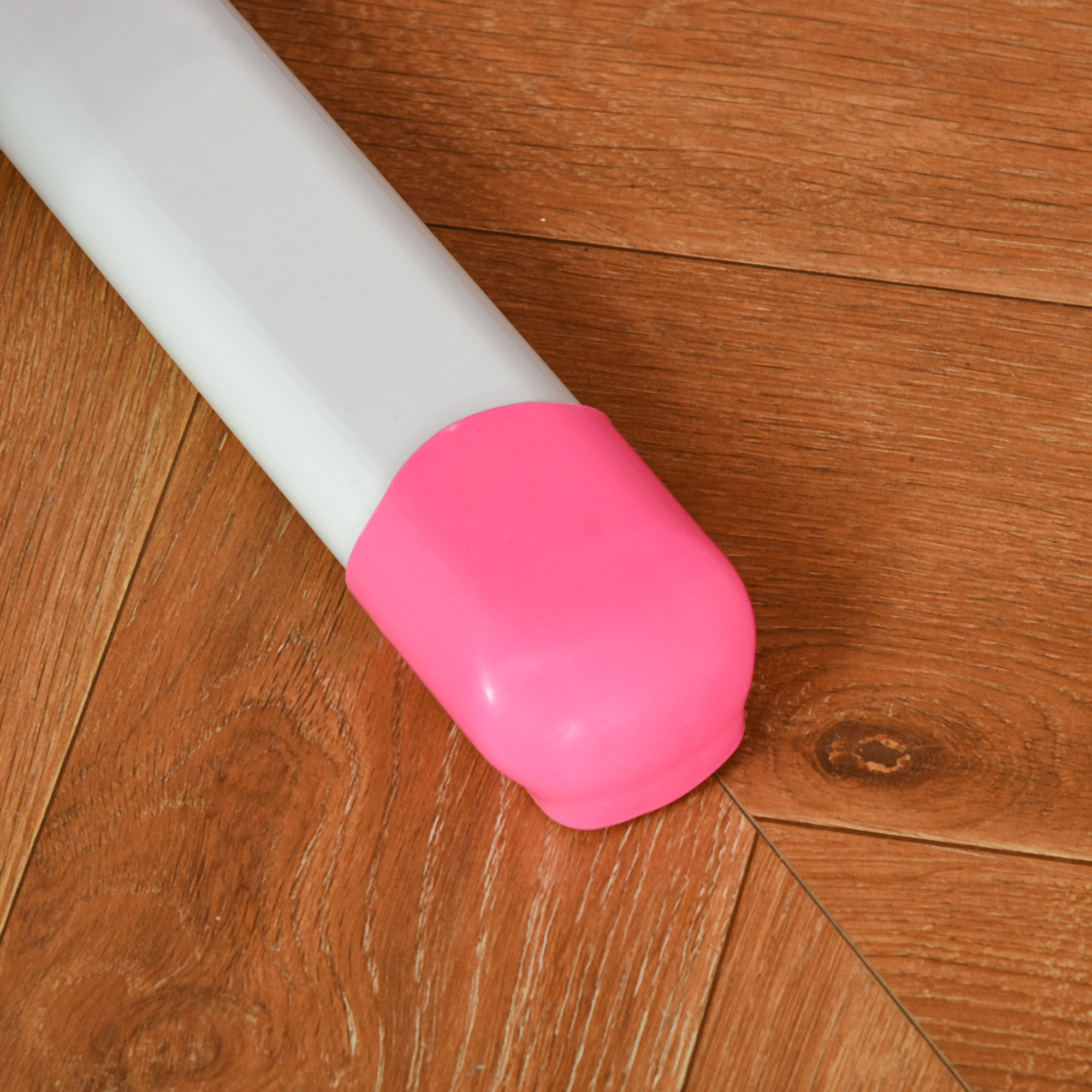Un tubo bianco con un tappo rosa poggia su un pavimento in legno. Il pavimento ha un motivo a venature marroni.