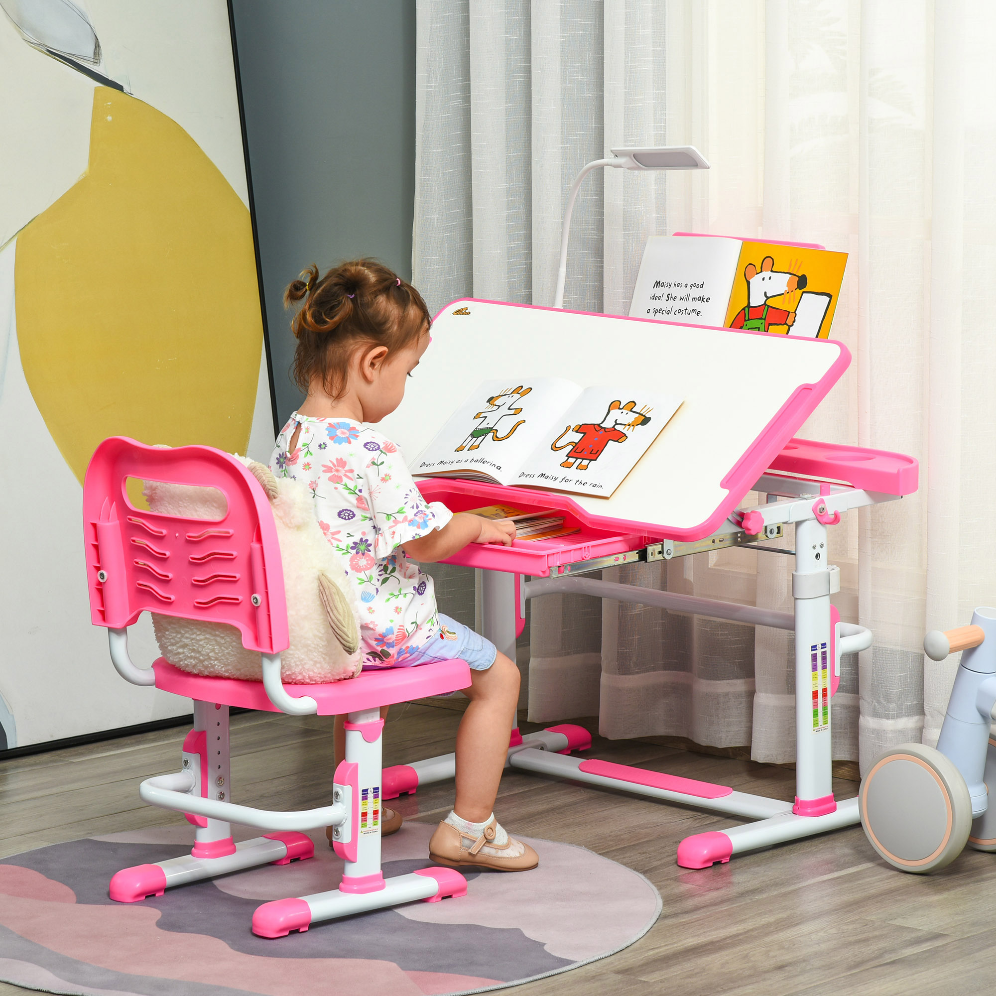 Una bambina è seduta a una scrivania rosa, che legge un libro. Un peluche è sulla sedia rosa. Una lampada e una finestra sono sullo sfondo.