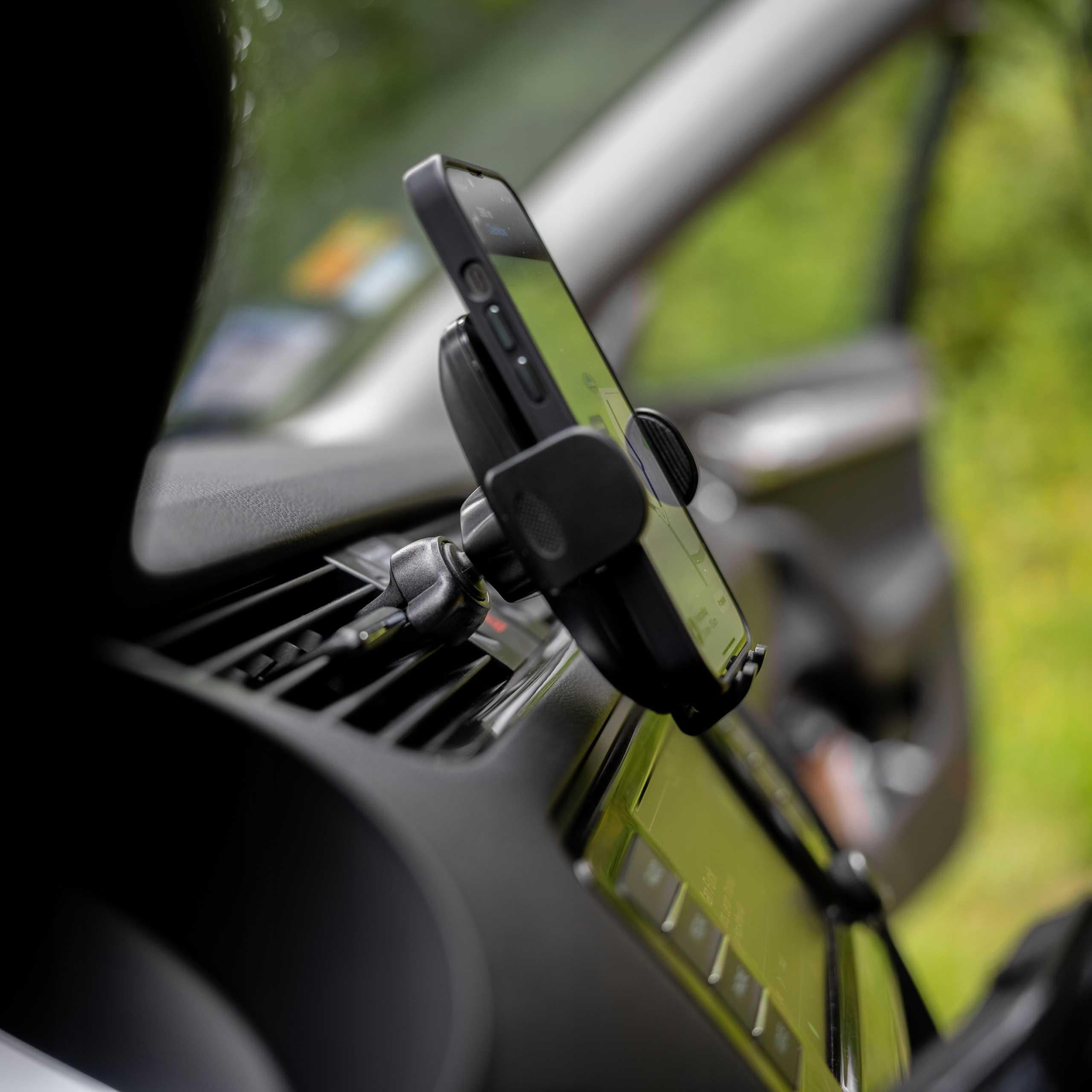 Smartfon zamontowany na desce rozdzielczej samochodu. Telefon wyświetla mapę. Tło jest rozmyte zielone.