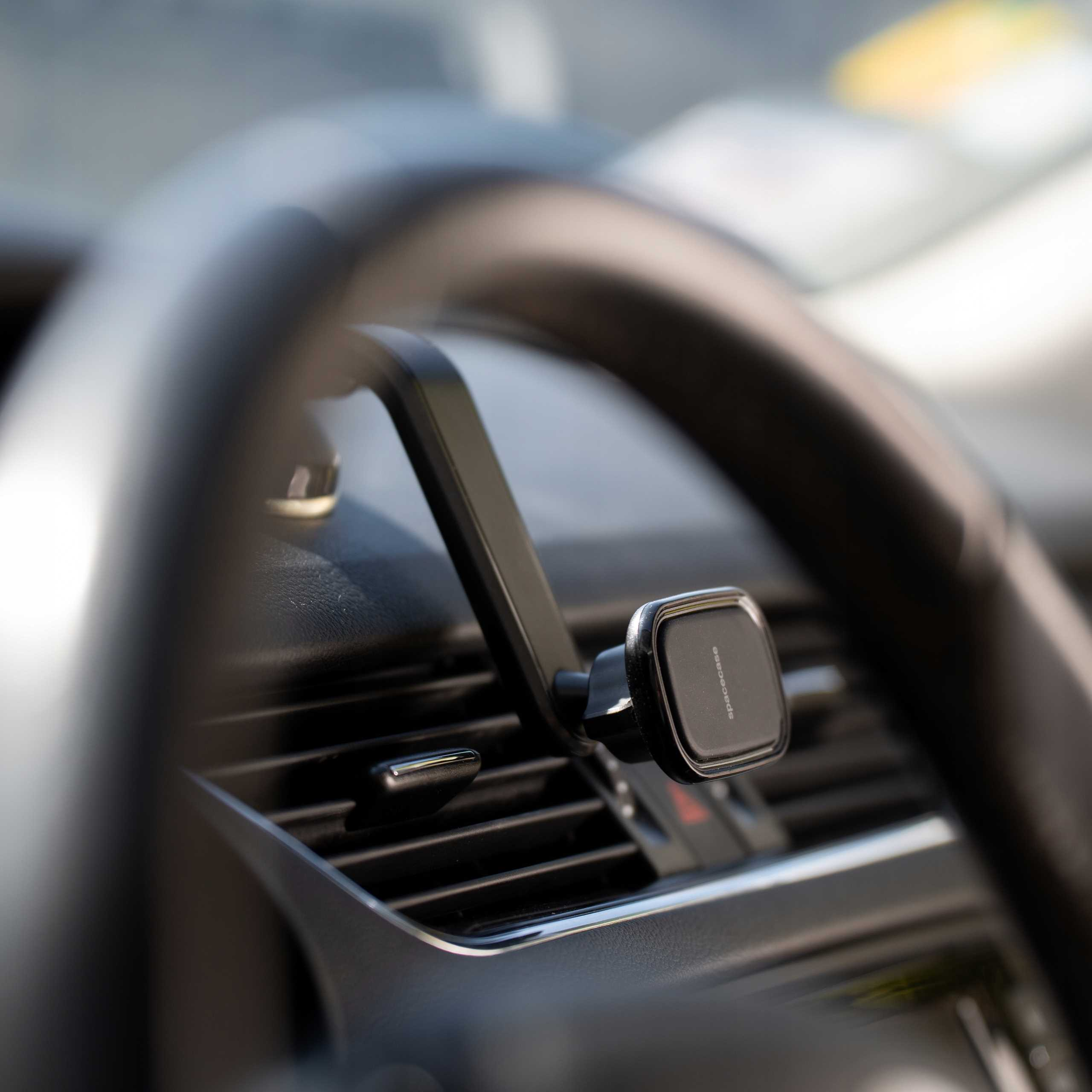 Wnętrze samochodu z uchwytem na telefon przymocowanym do kratki wentylacyjnej. Widoczna kierownica.