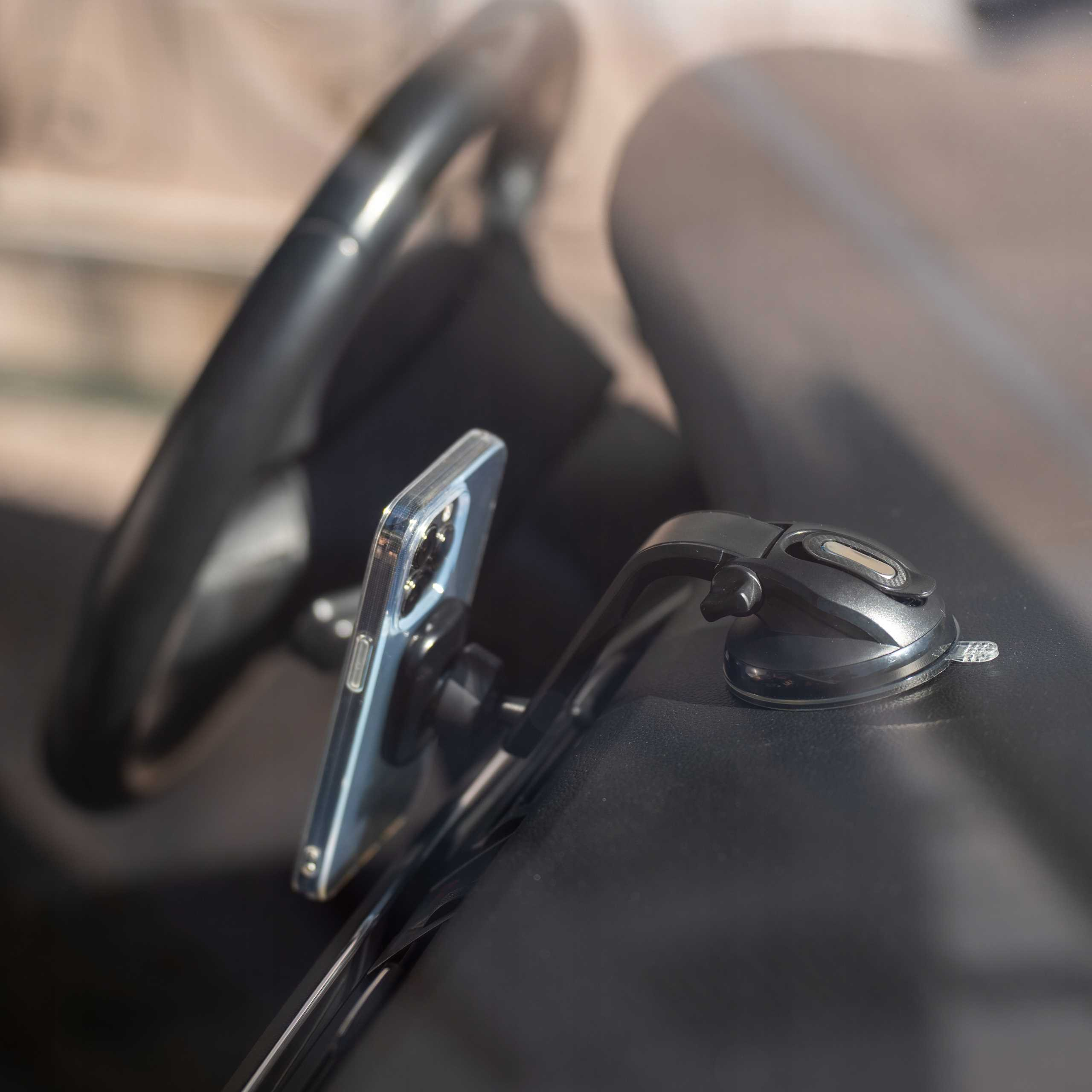 Telefon jest zamontowany na przedniej szybie samochodu za pomocą przyssawki. Kierownica widoczna w tle.