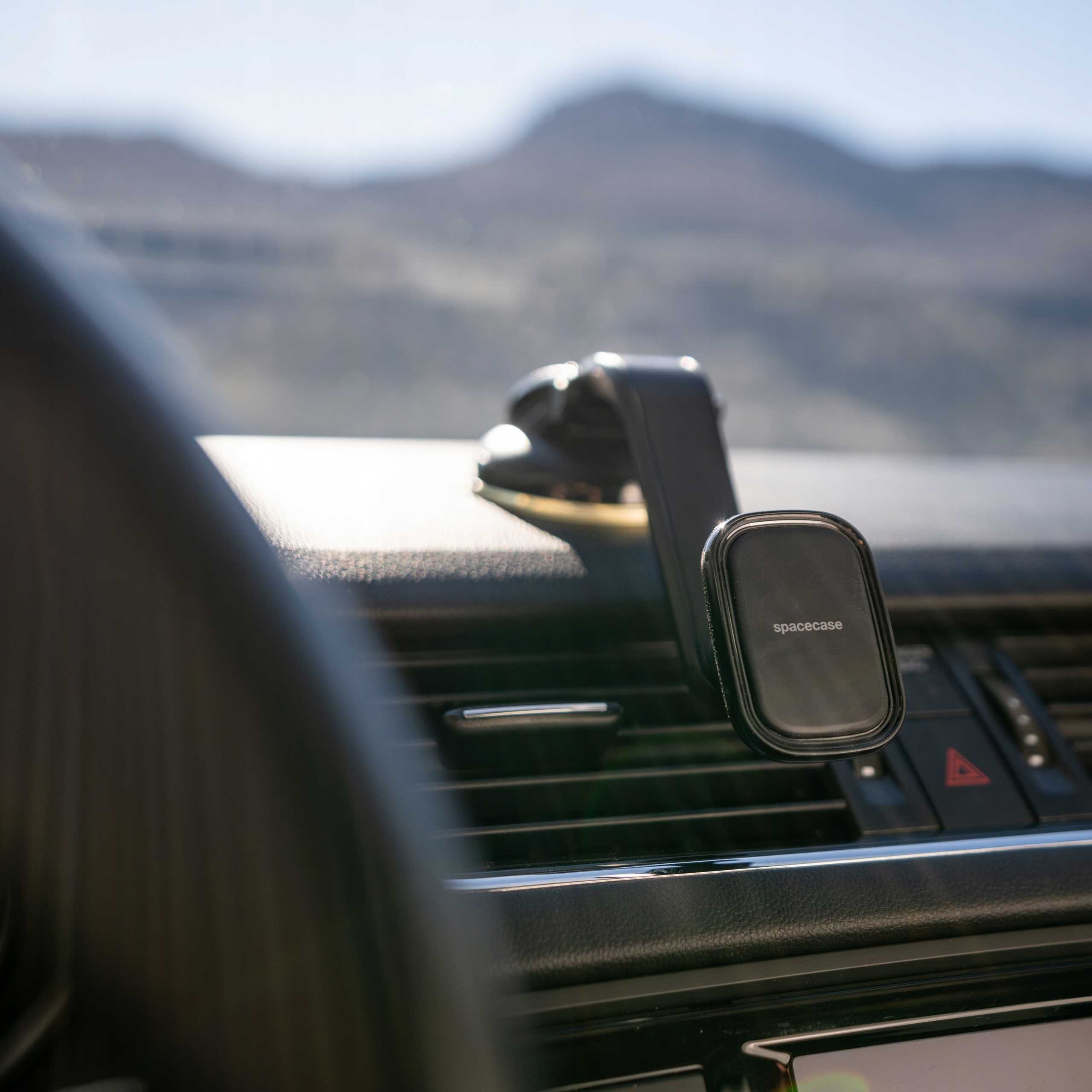 Czarny uchwyt na telefon w samochodzie z widokiem na góry w tle. Na uchwycie napis 'spacecase'.