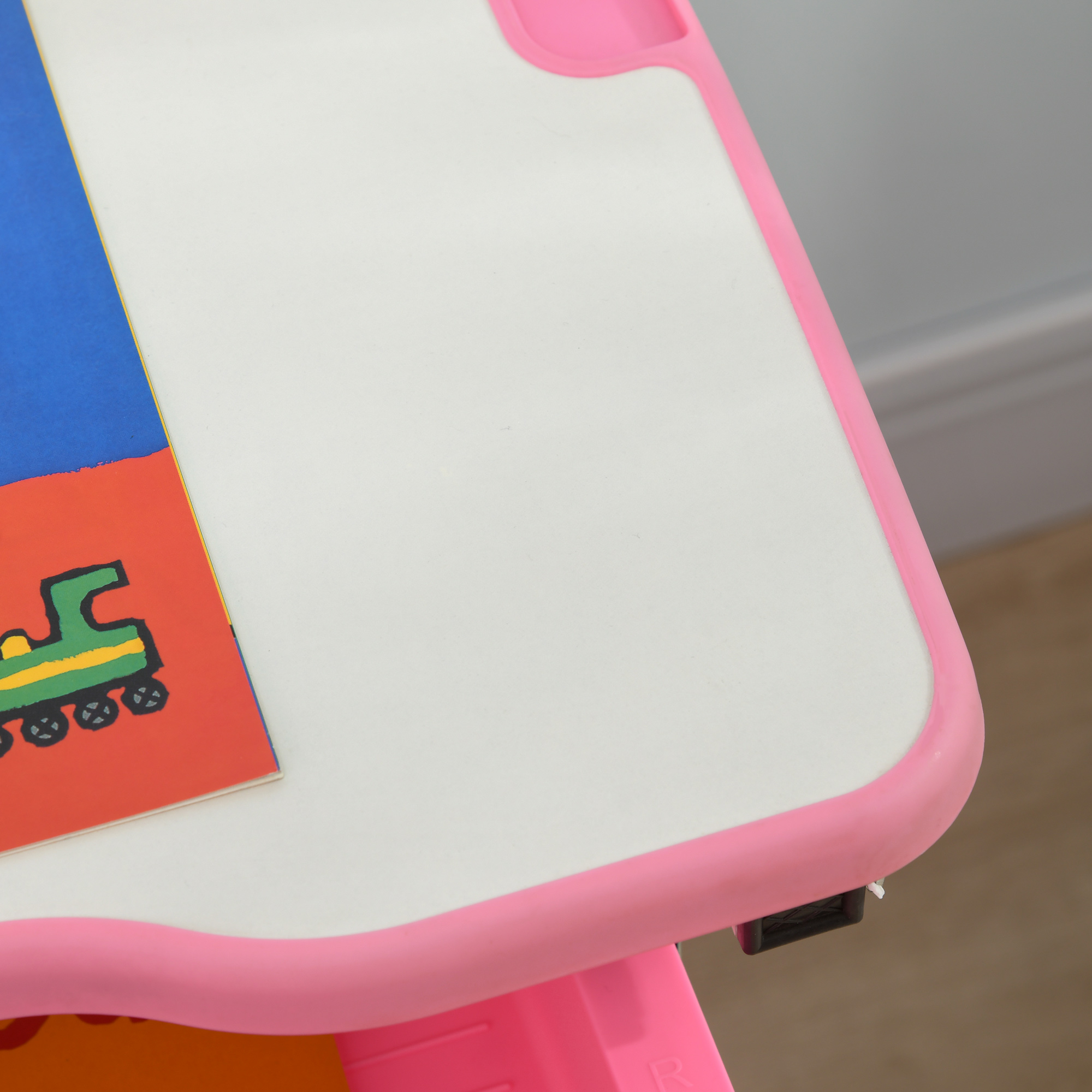 Primo piano di un tavolo rosa e bianco con un libro colorato che mostra un treno verde. Il tavolo ha un bordo rosa.