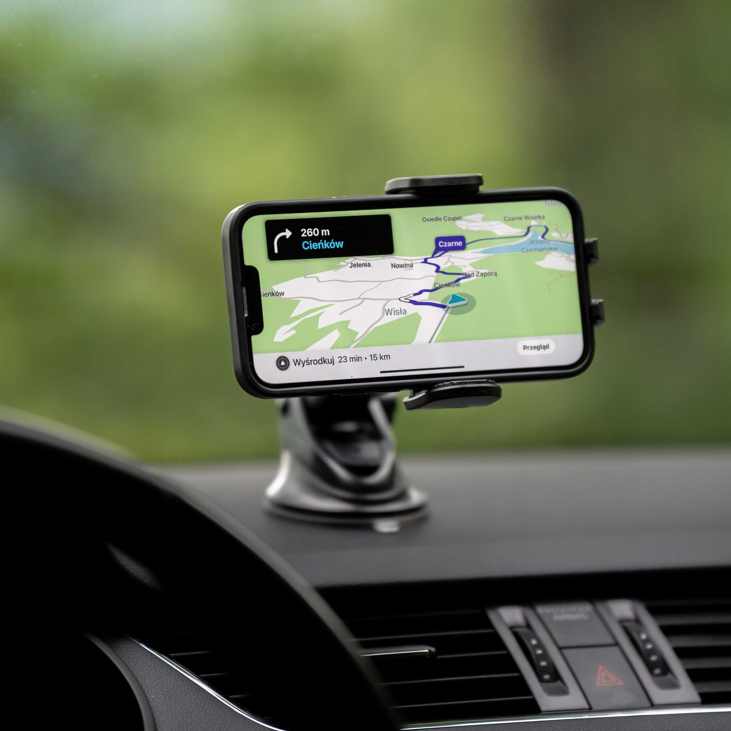 Telefon w uchwycie samochodowym wyświetla mapę z trasą do Cieńków. Tło jest rozmyte zielone.