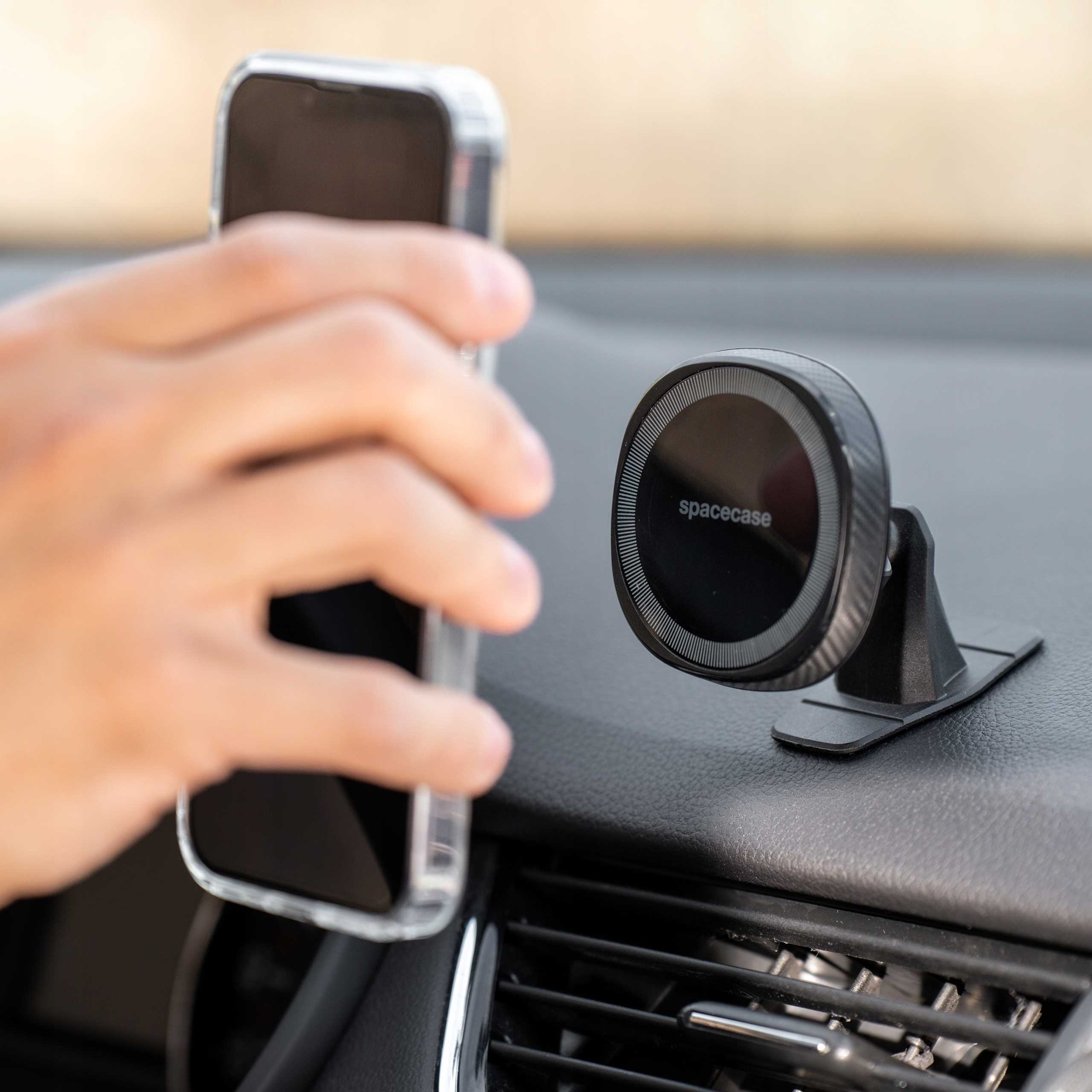 Ręka umieszcza telefon na uchwycie samochodowym. Uchwyt jest czarny, z okrągłą głowicą magnetyczną.