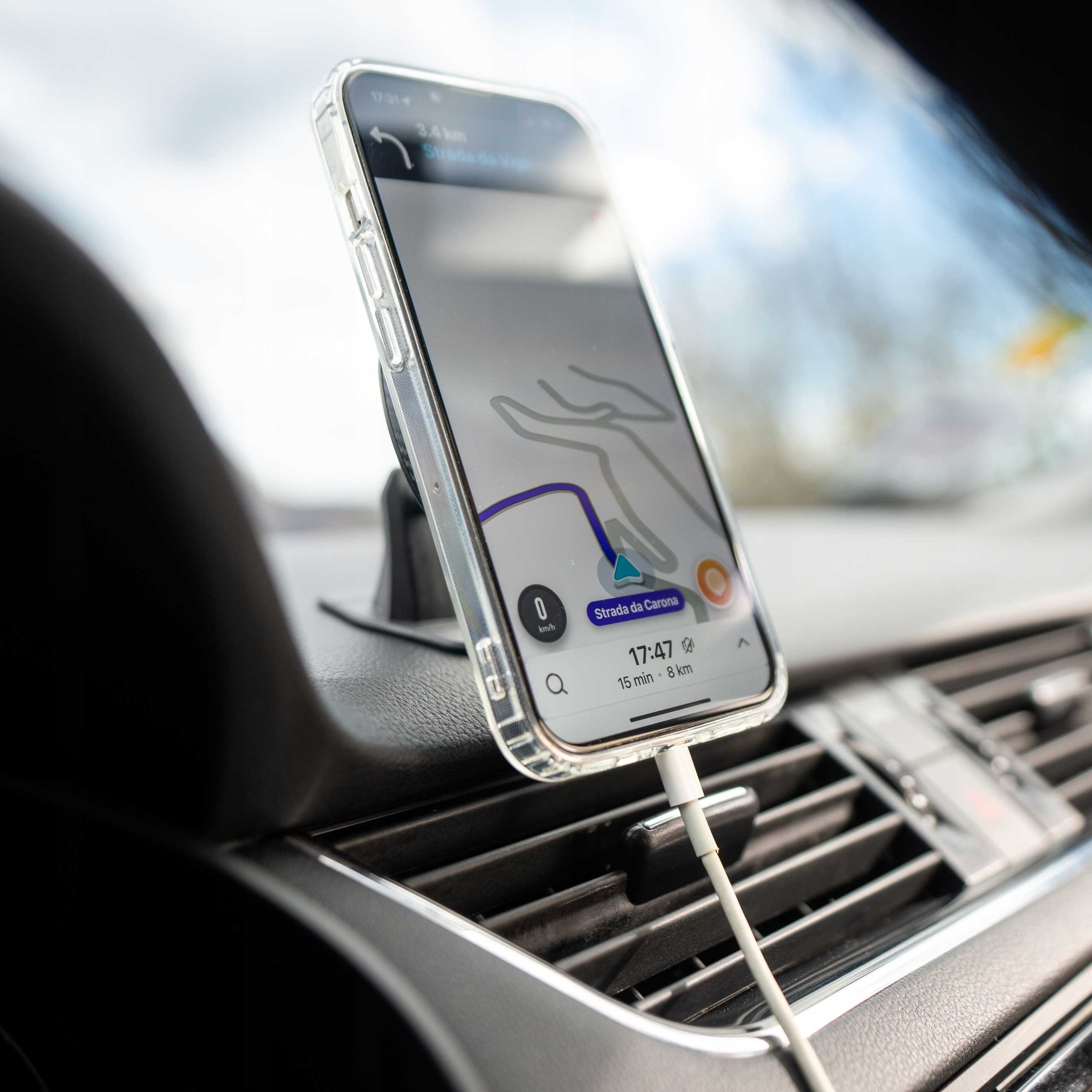 Telefon w samochodzie pokazuje aplikację nawigacyjną. Telefon jest ładowany. Widoczna jest deska rozdzielcza i wentylacja.