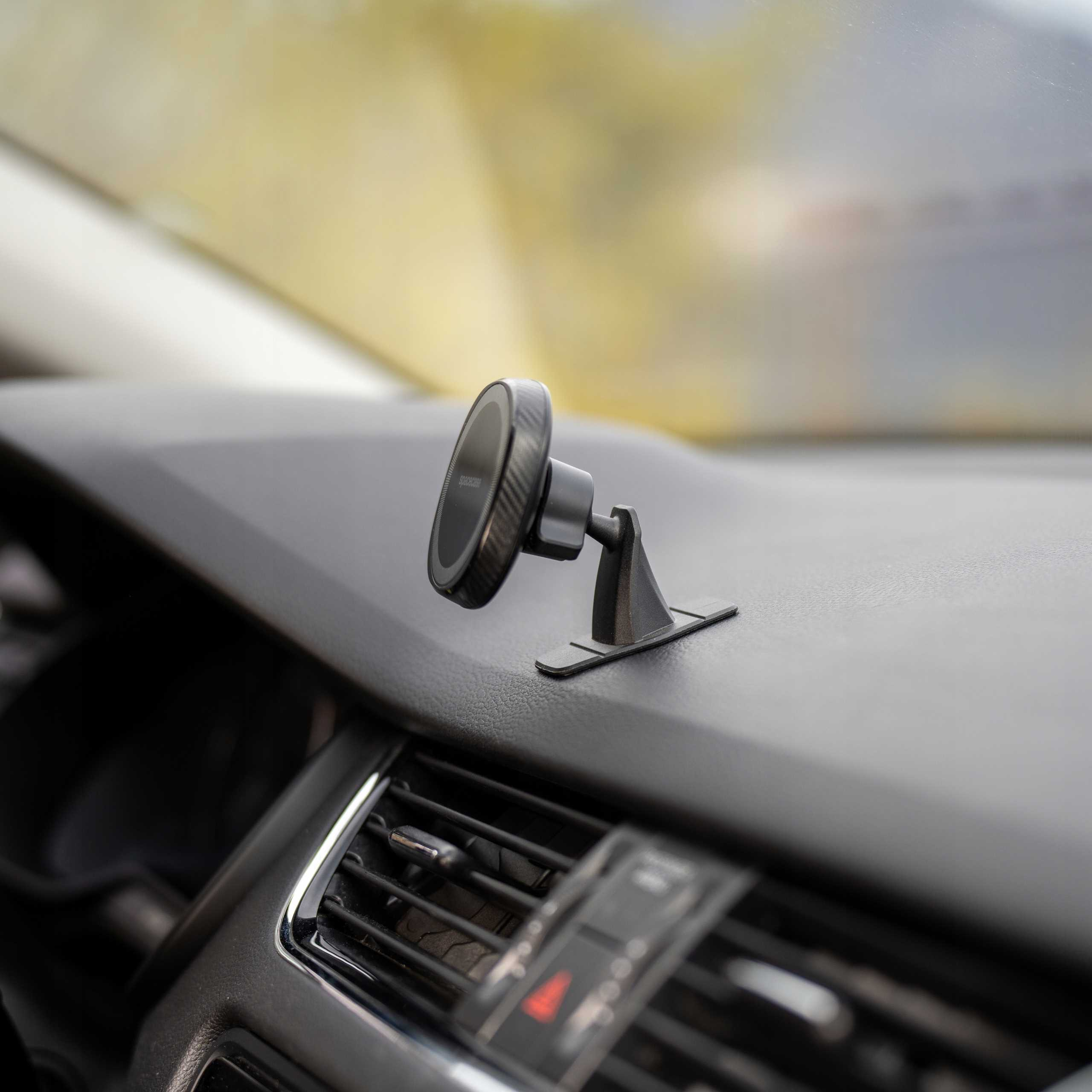 Czarny uchwyt na telefon zamontowany na desce rozdzielczej samochodu. Rozmyte tło wnętrza.