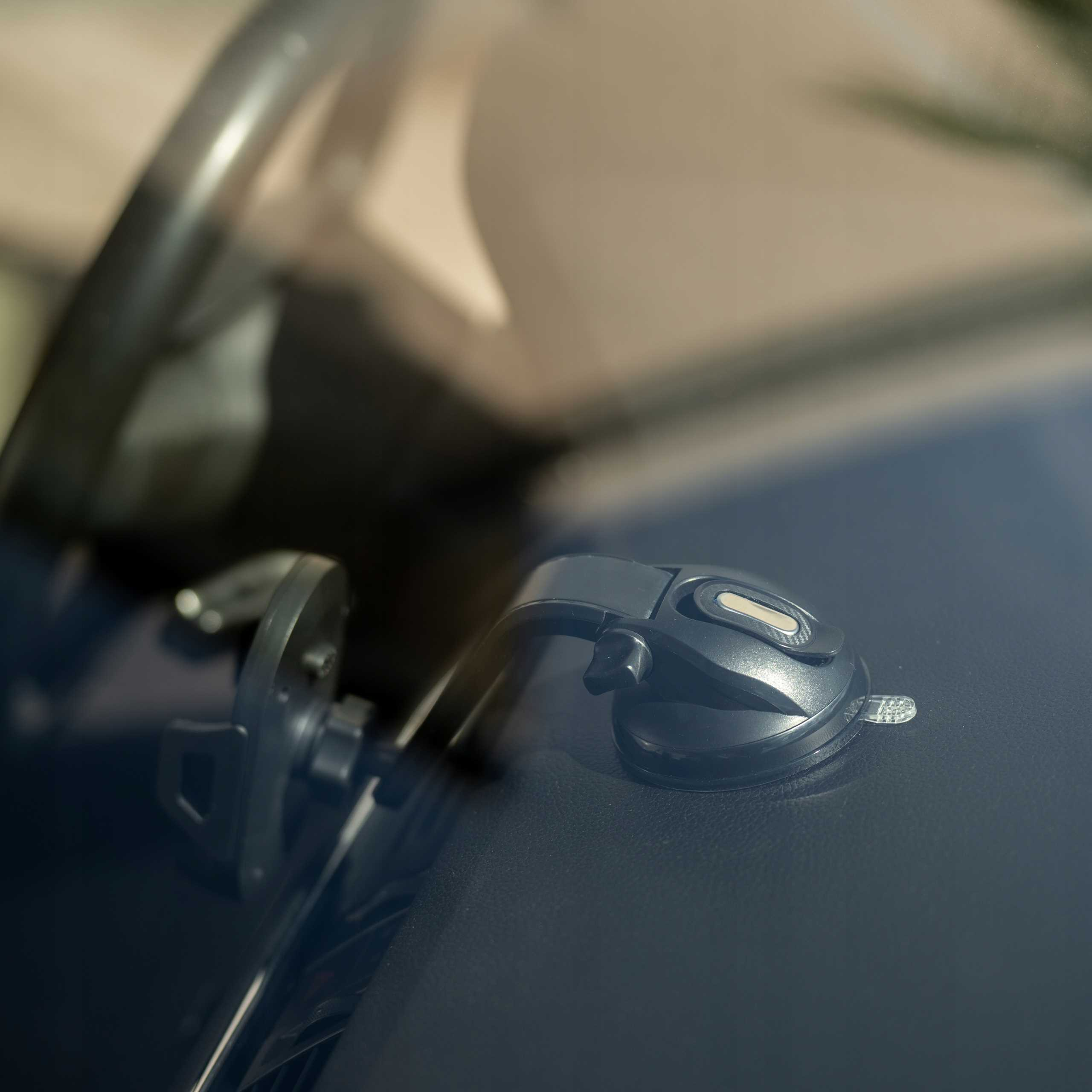 Deska rozdzielcza samochodu z uchwytem na telefon przymocowanym do przedniej szyby. Kierownica widoczna w tle.