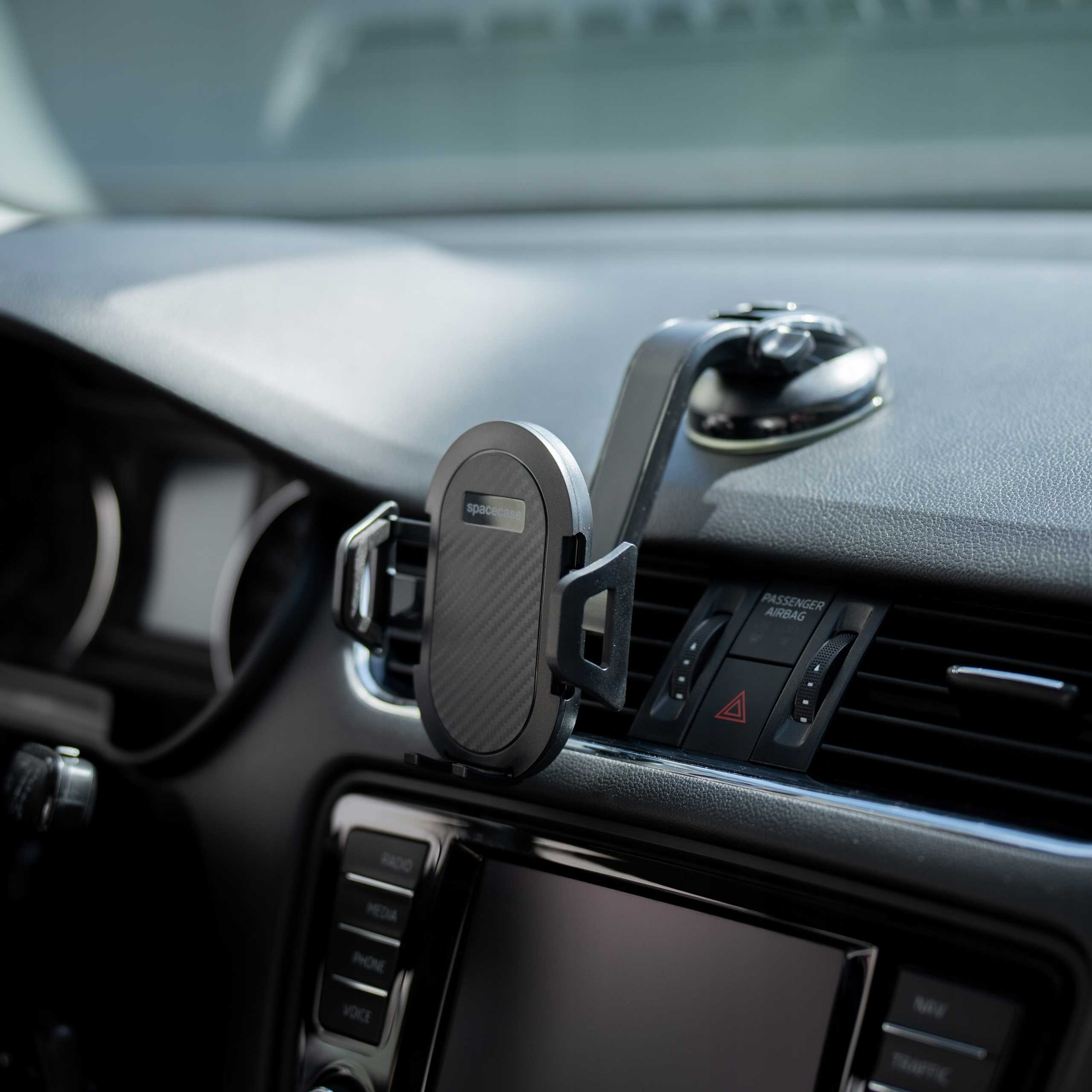 Deska rozdzielcza samochodu z uchwytem na telefon. Uchwyt jest przymocowany do kratki wentylacyjnej. Widoczne radio i inne elementy sterujące.