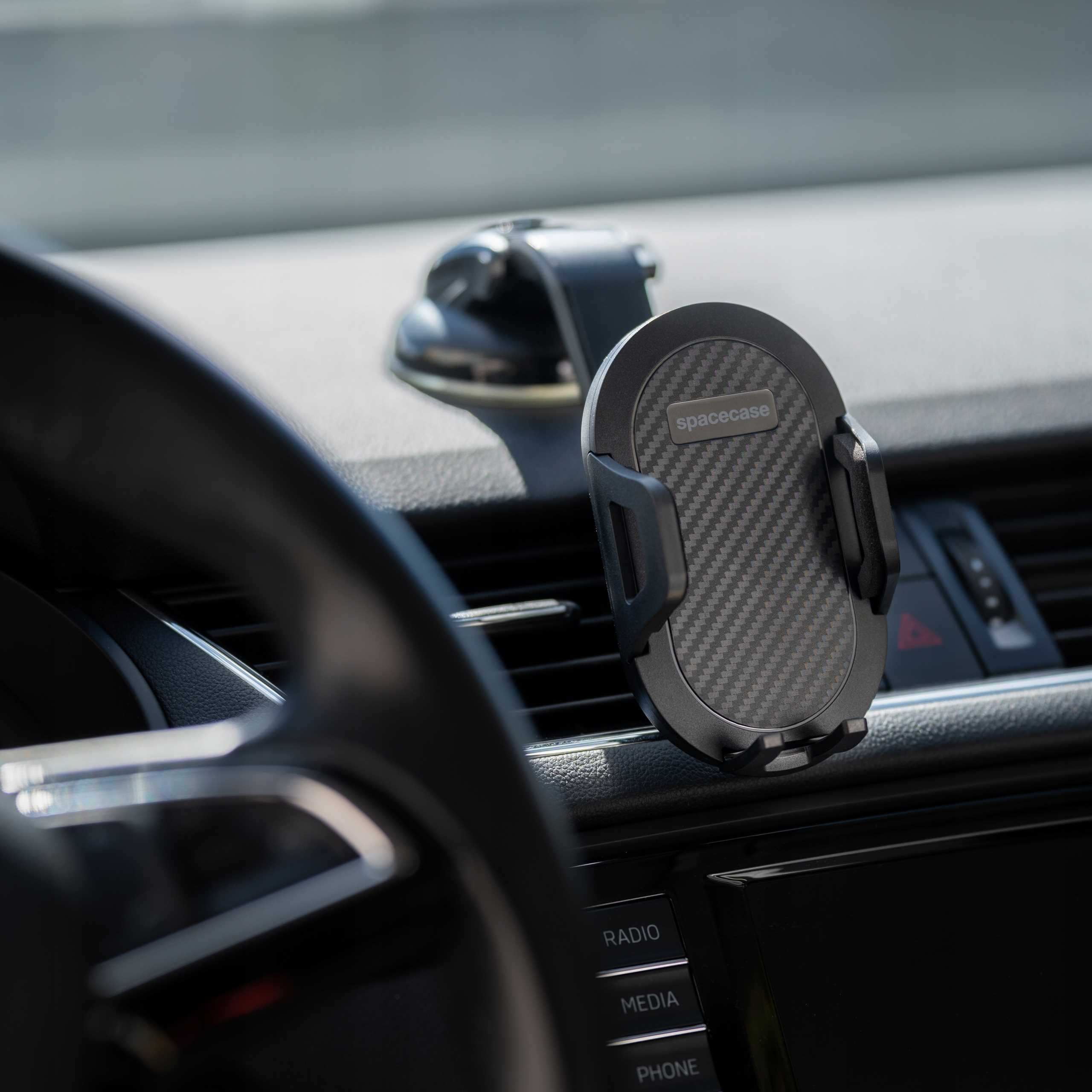 Deska rozdzielcza samochodu z uchwytem na telefon. Uchwyt jest na środku, ze wzorem z włókna węglowego. Kierownica po lewej.