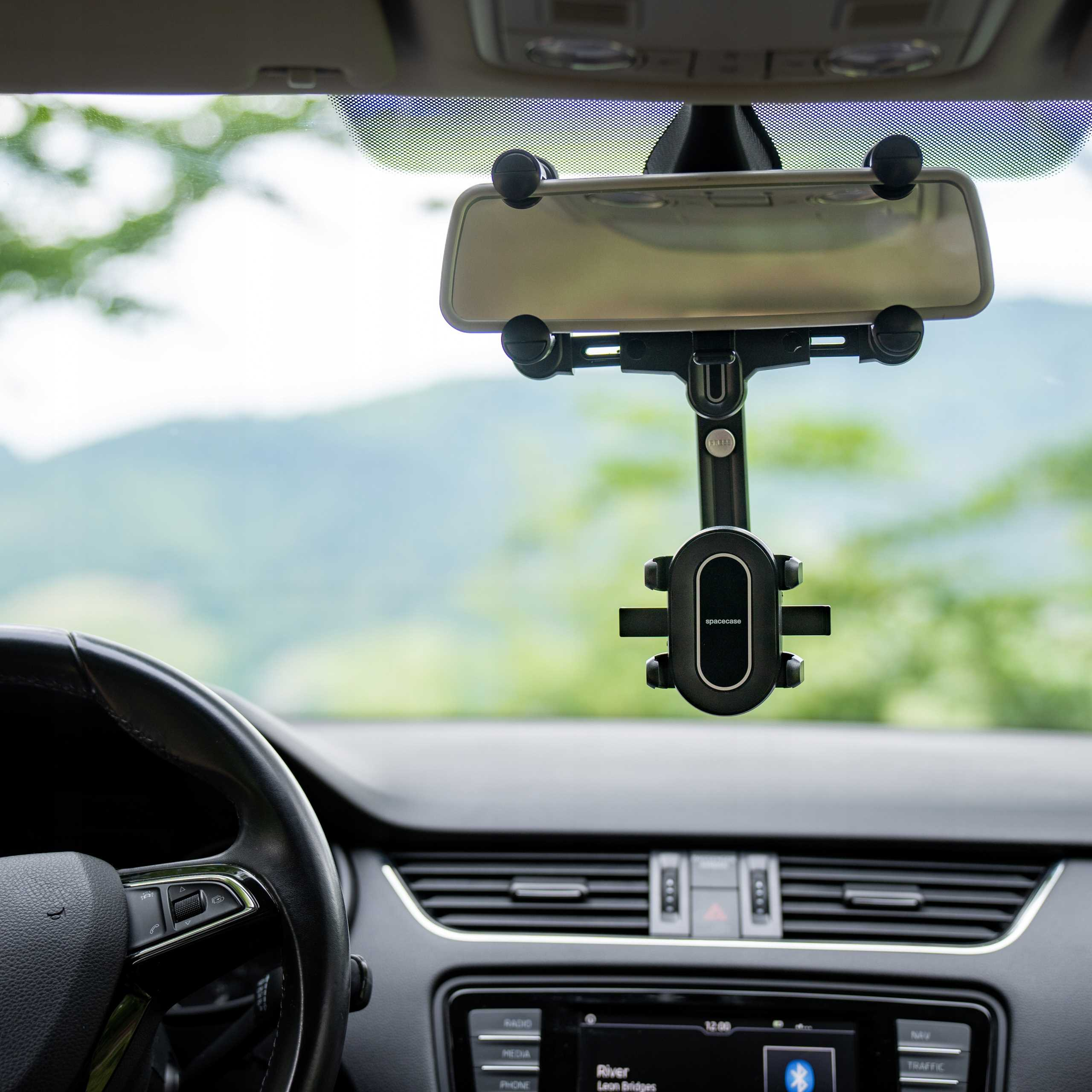 Ujęcie wnętrza samochodu. Uchwyt na telefon jest przymocowany do lusterka wstecznego. Deska rozdzielcza, kierownica na pierwszym planie.