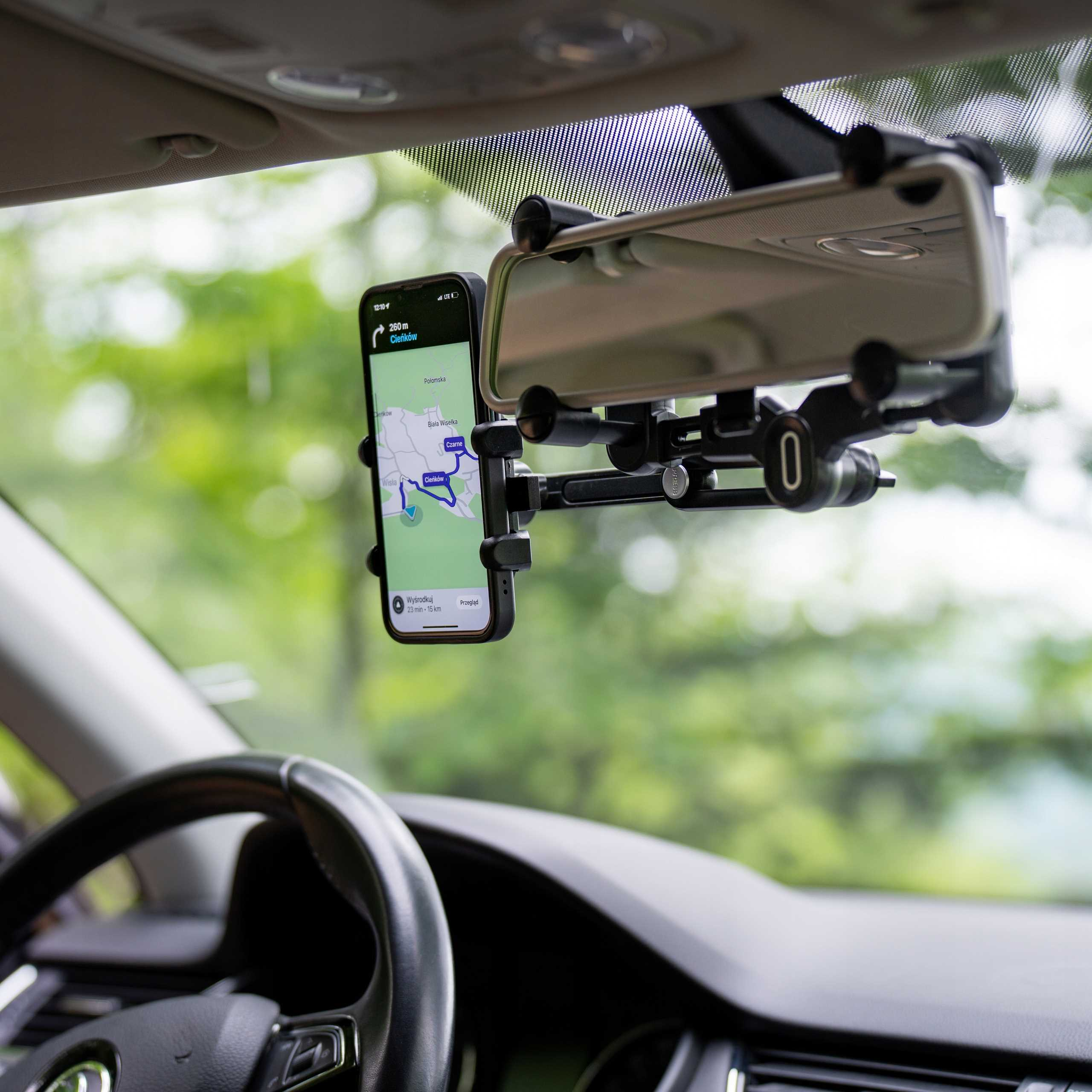 Telefon wyświetla mapę nawigacji w samochodzie. Widoczne są również kierownica i lusterko wsteczne.