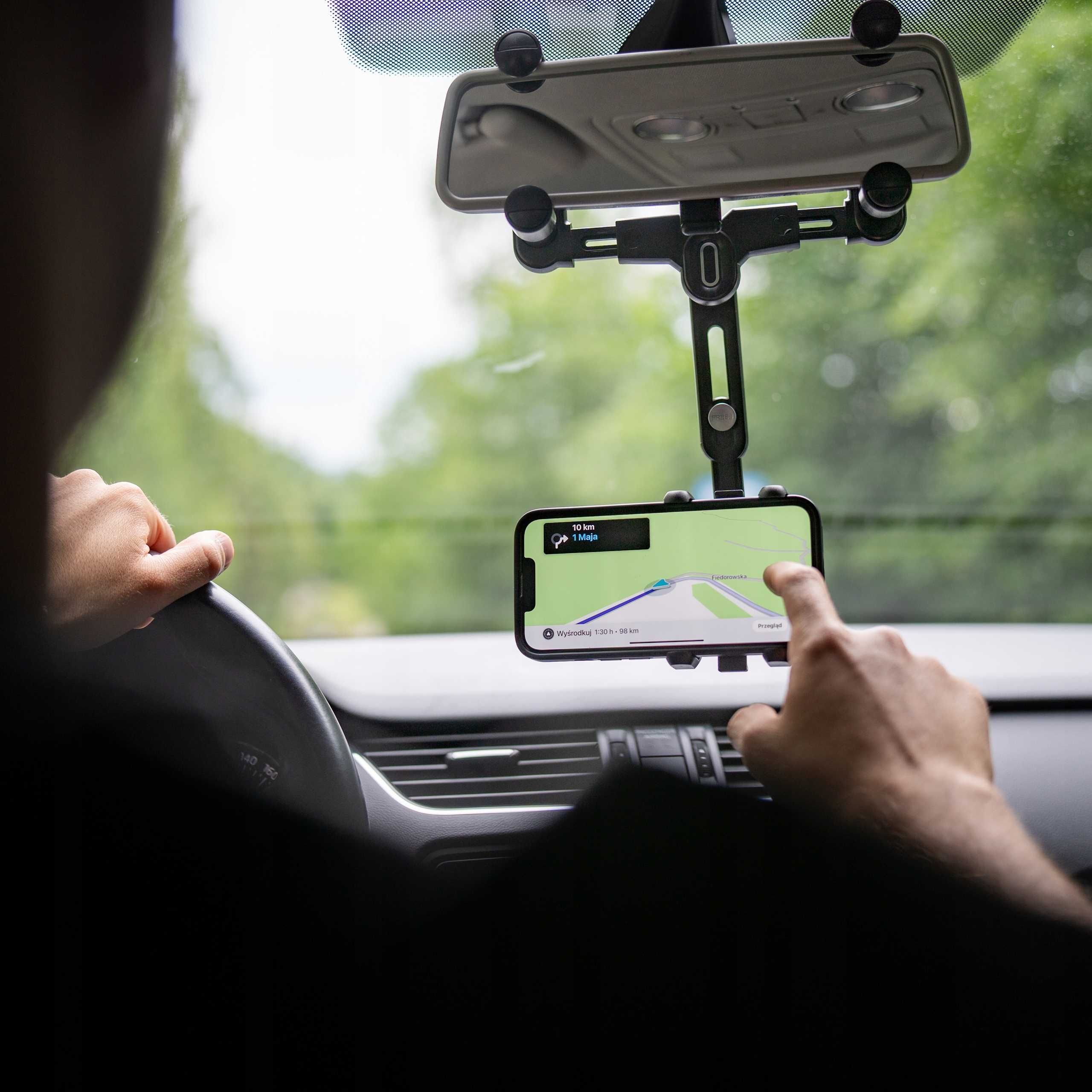 Osoba w samochodzie korzysta z aplikacji nawigacyjnej w telefonie przymocowanym do uchwytu. Osoba dotyka ekranu.