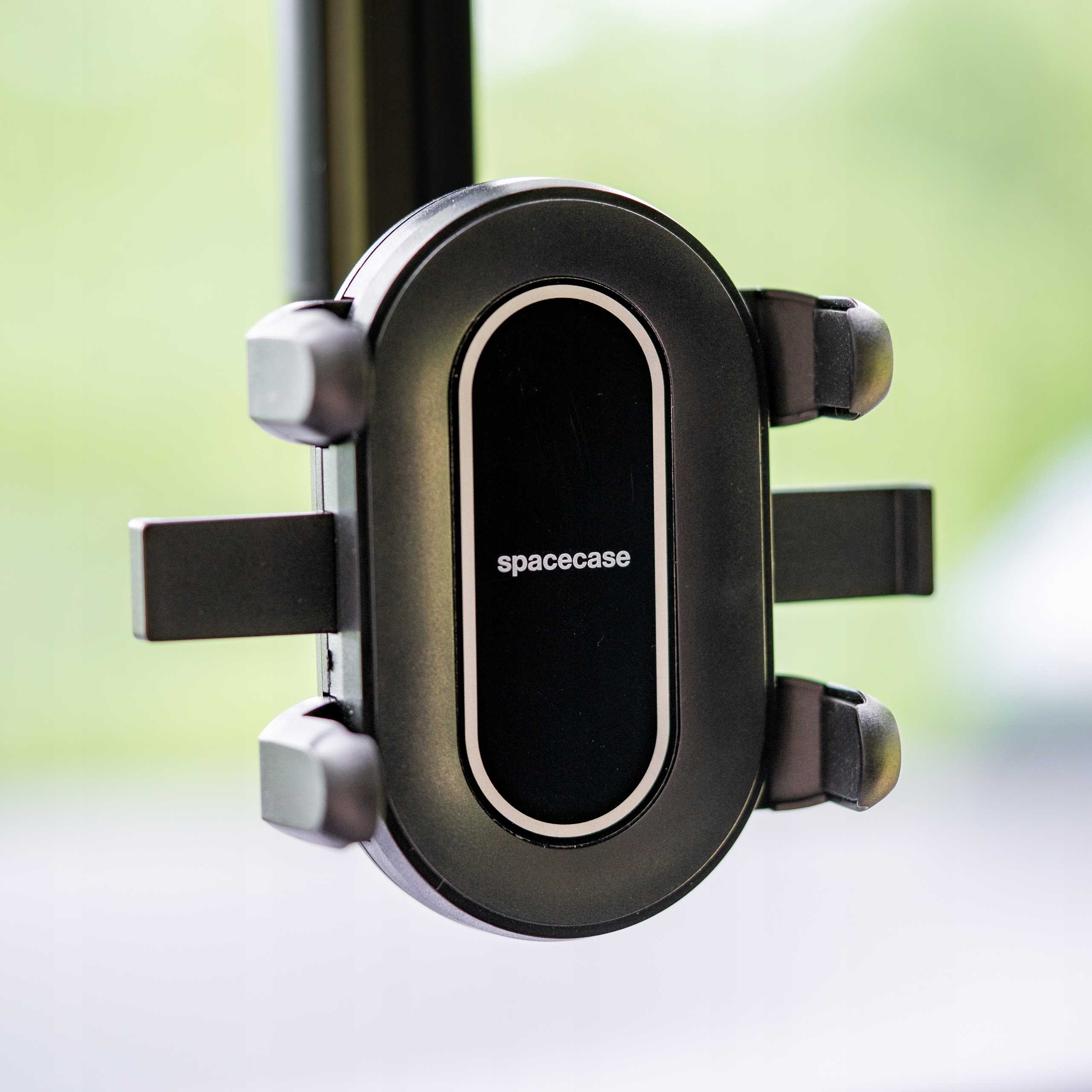 Czarny uchwyt do telefonu Spacecase. Ma owalne centrum z nazwą marki. Tło jest rozmyte zielone i białe.