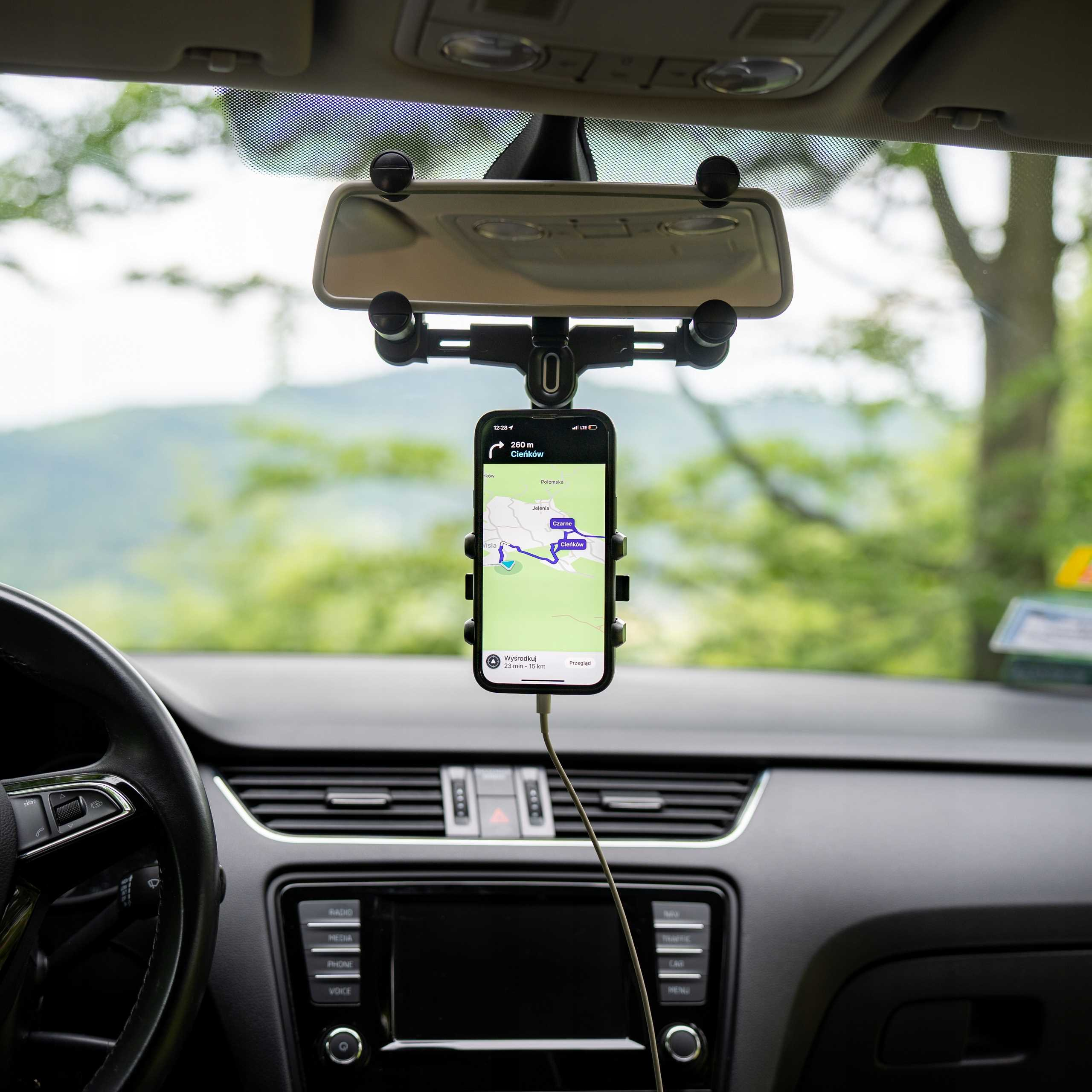 Wewnątrz samochodu telefon wyświetla mapę z nawigacją, zamontowany na uchwycie. Widoczna kierownica i deska rozdzielcza.