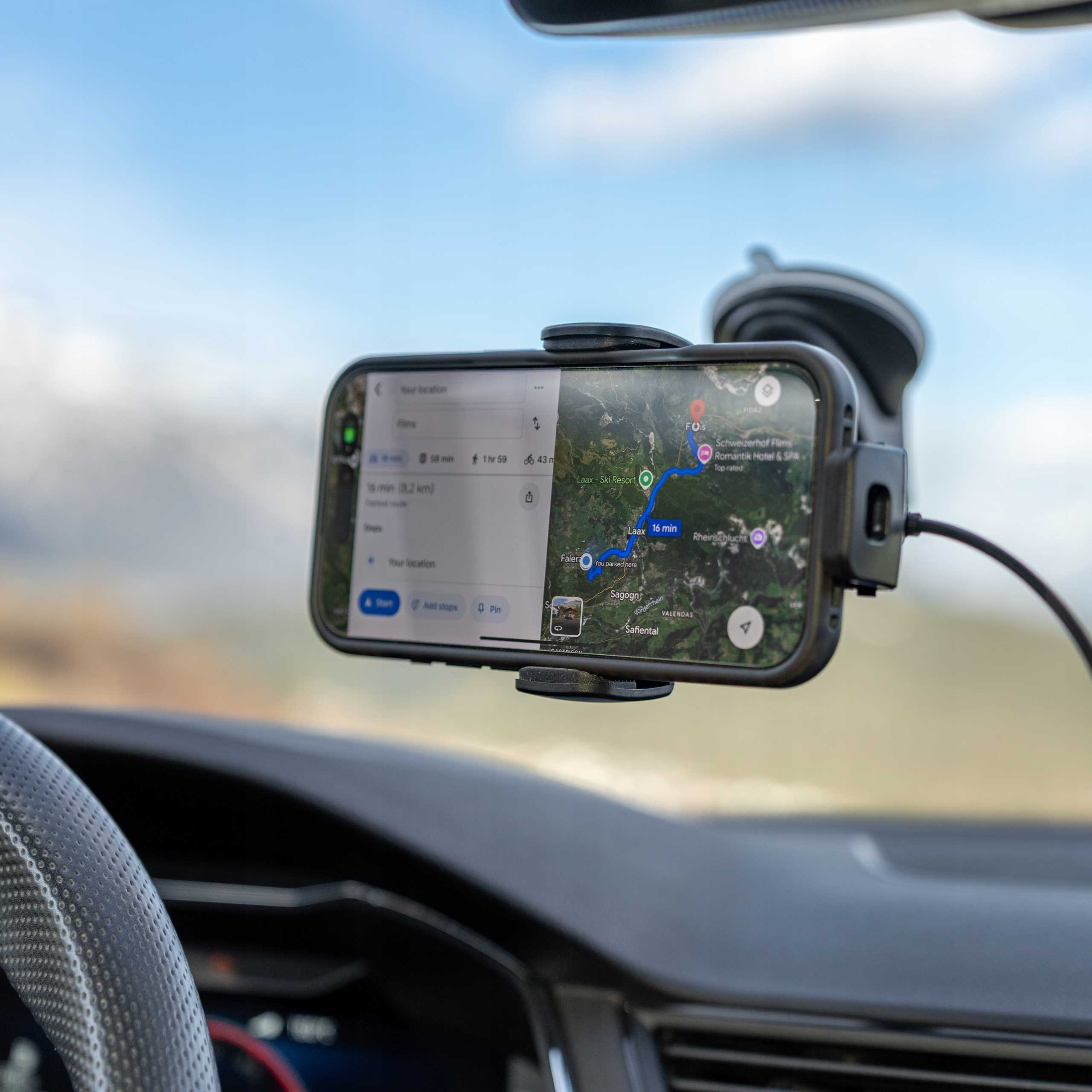 Telefon wyświetla mapę w samochodzie. Telefon jest zamontowany na przedniej szybie, pokazując trasę. Niebo jest niebieskie.