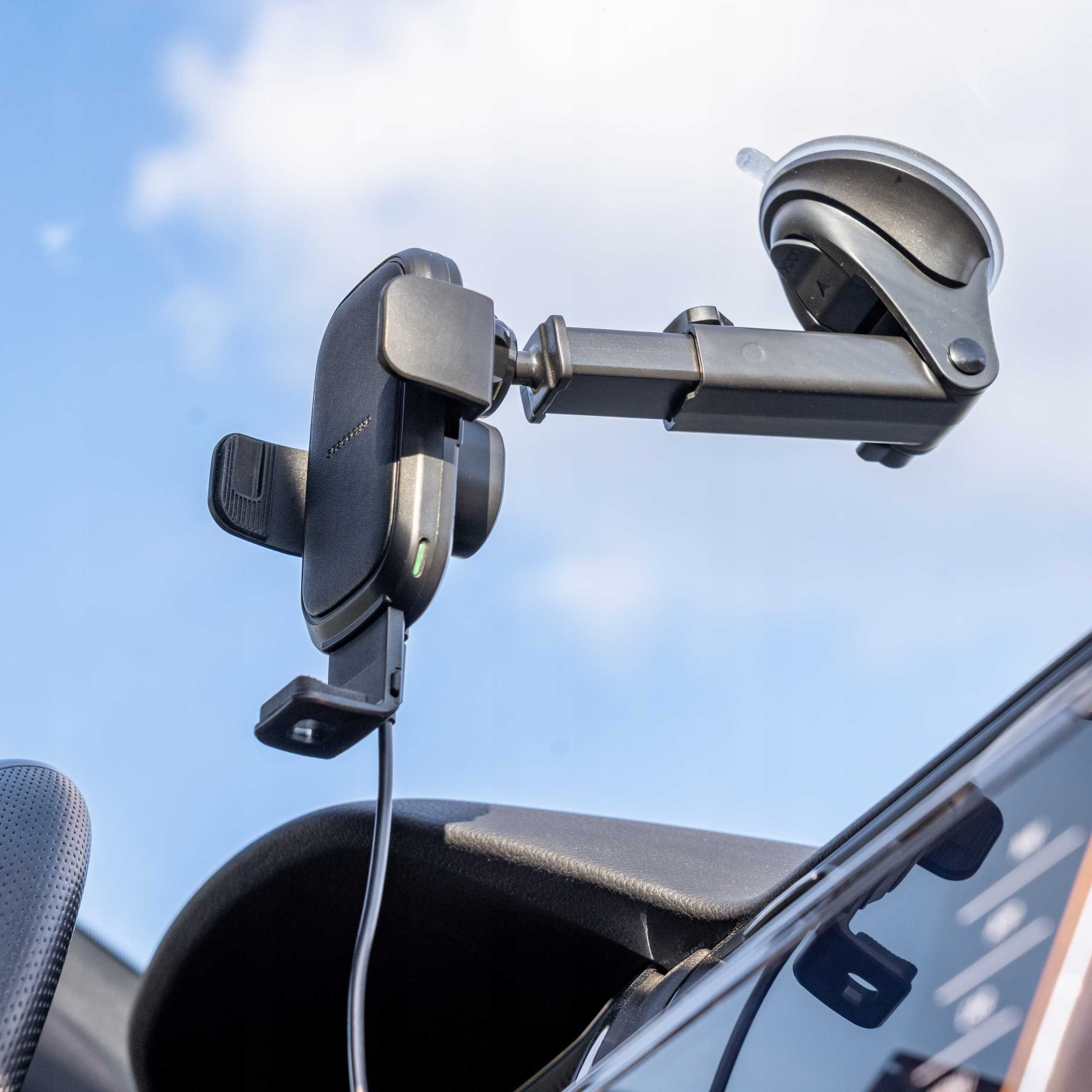 Czarny uchwyt na telefon samochodowy zamontowany na przedniej szybie z błękitnym niebem w tle.