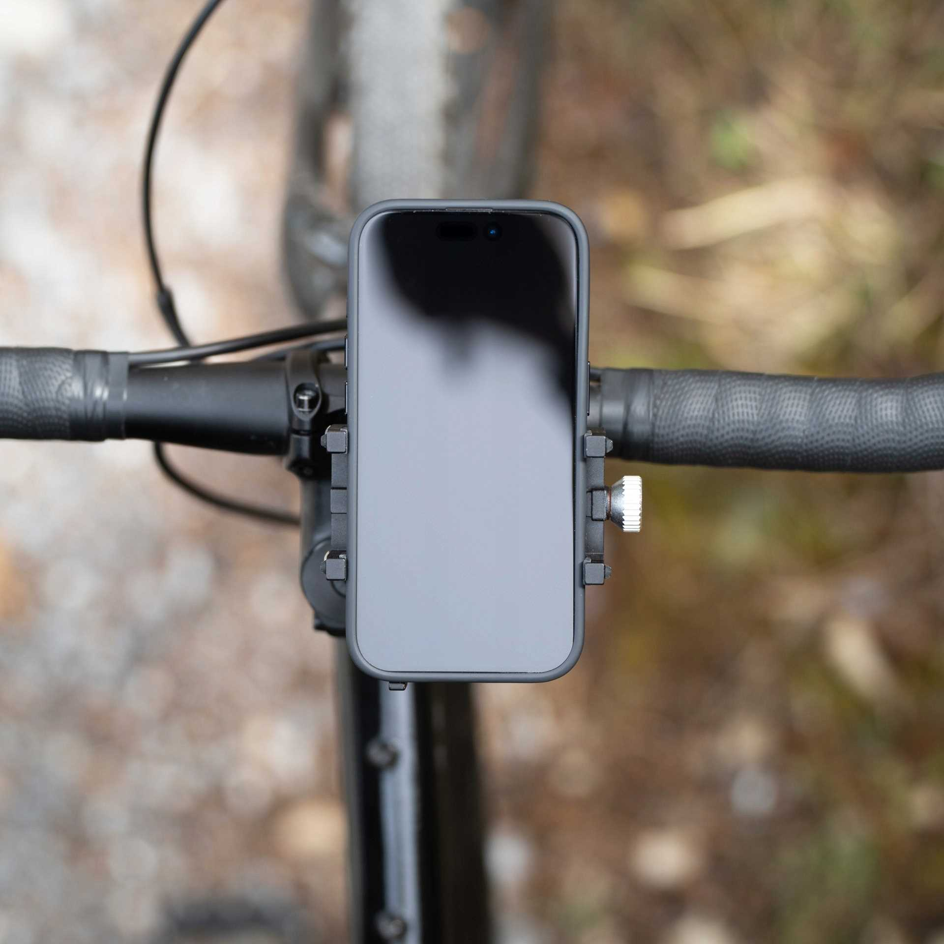 Smartfon zamontowany na kierownicy roweru. Telefon jest w czarnym etui. Tło jest rozmyte.