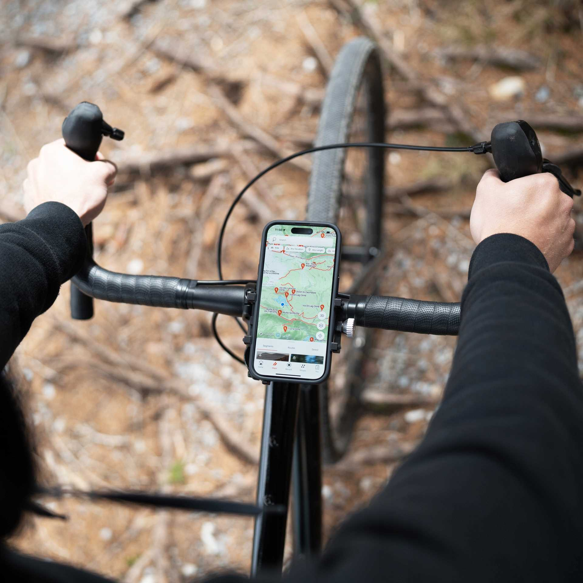 Ręce rowerzysty na kierownicy z telefonem z mapą. Tło to rozmyty las.