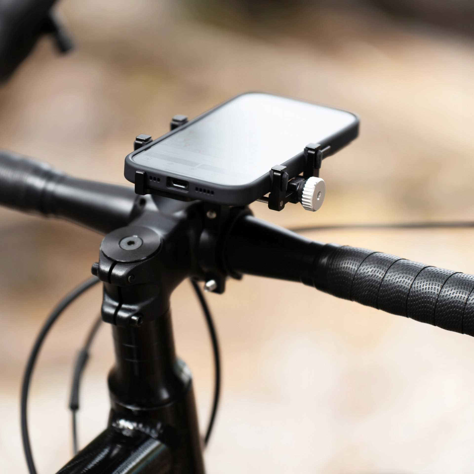 Telefon zamontowany na kierownicy roweru. Telefon jest czarny, kierownica jest czarna, a tło jest rozmyte.
