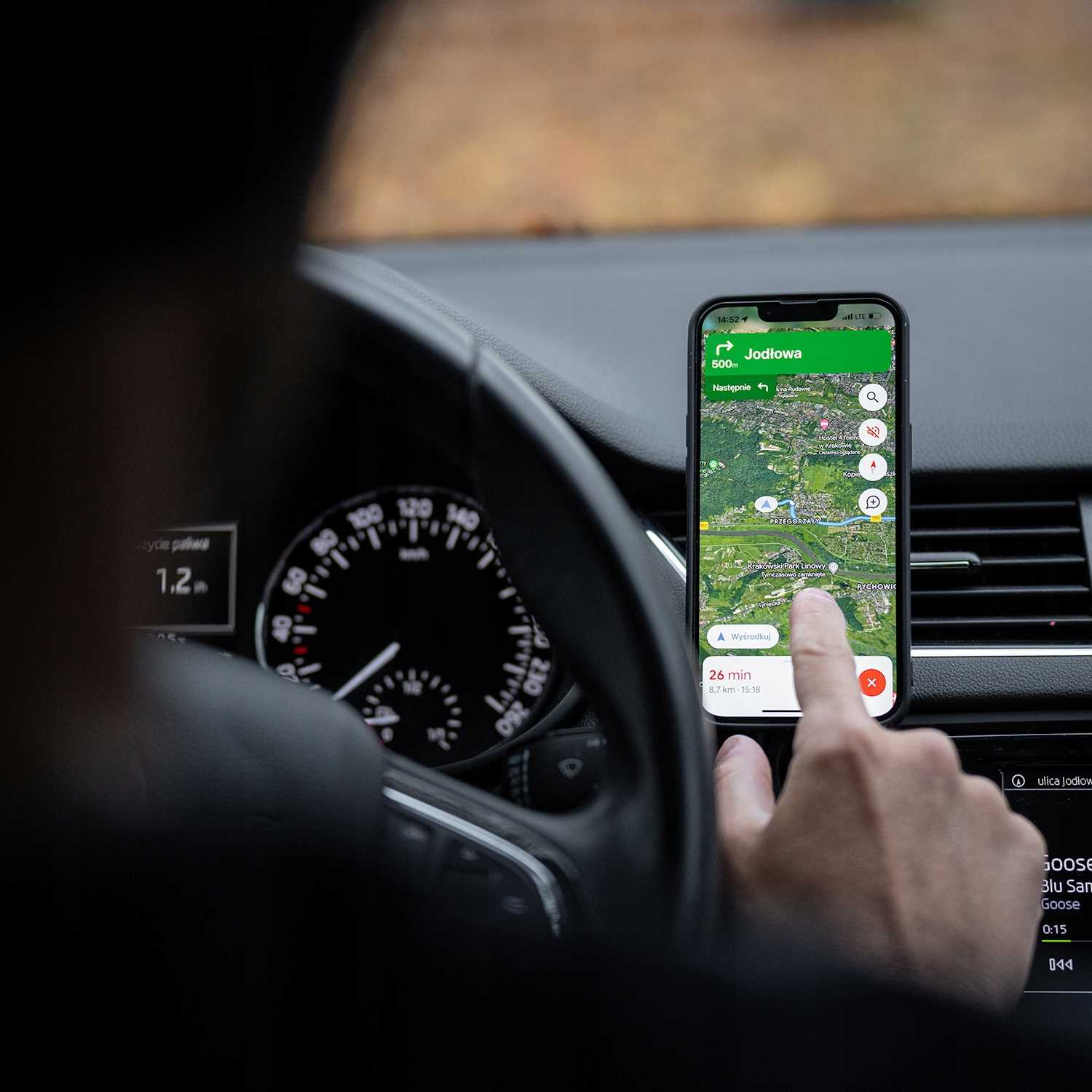 Osoba w samochodzie korzysta z telefonu z mapą. Ekran pokazuje trasę do Jodłowej, ze szczegółami nawigacji.