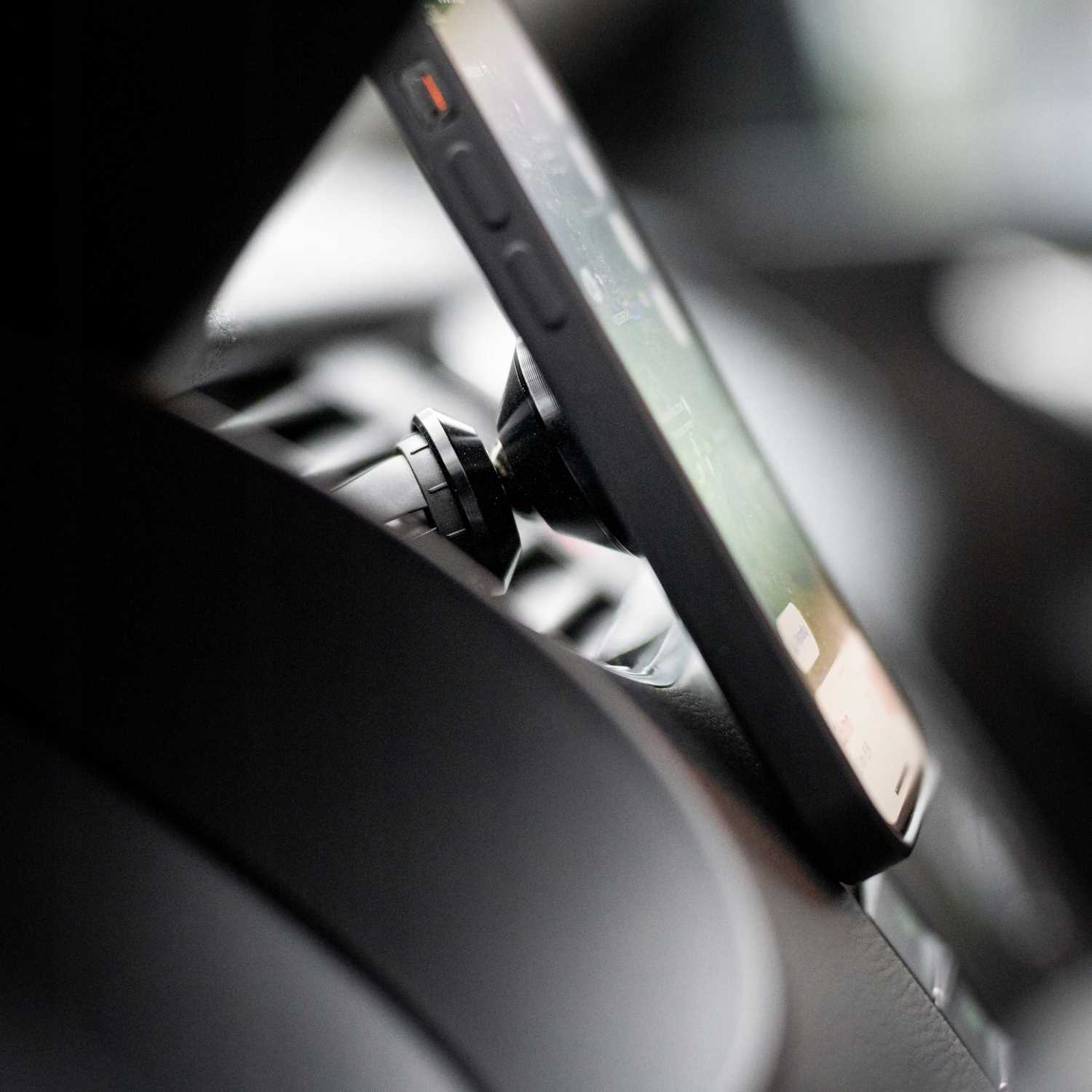 Smartfon zamontowany na czarnej desce rozdzielczej. Ekran widoczny, wnętrze ciemne.