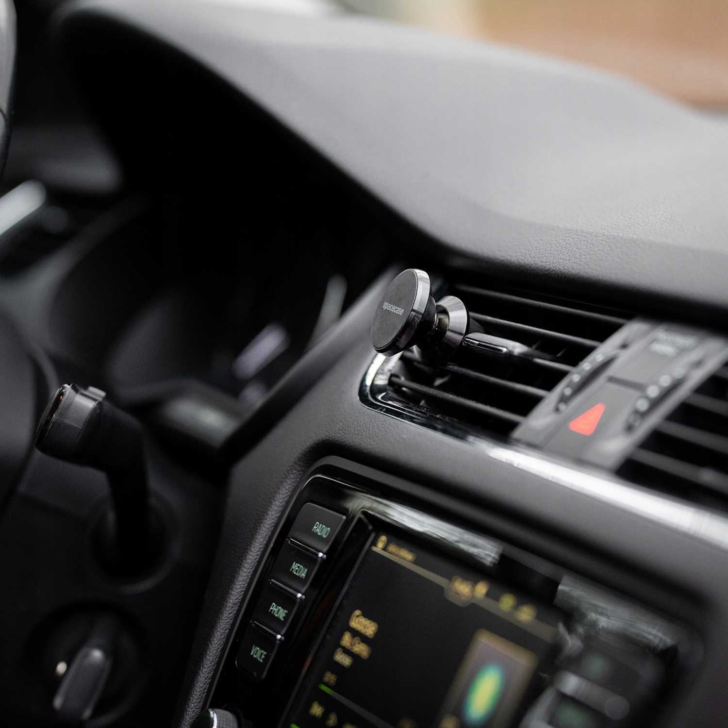 Wnętrze samochodu z uchwytem na telefon przymocowanym do kratki wentylacyjnej. Widoczne przyciski radia i multimediów. Ekran wyświetla Google i inne informacje.