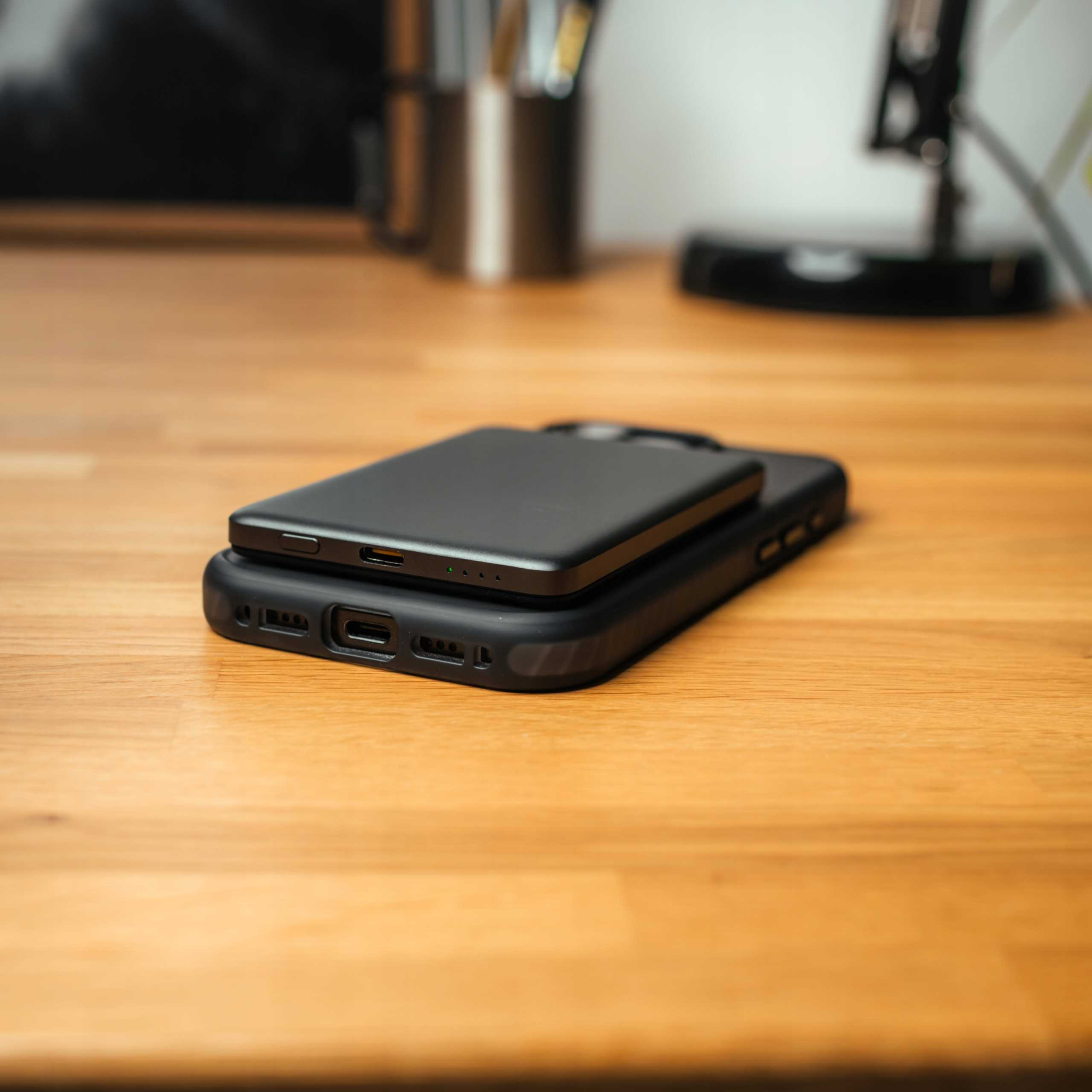 Czarny telefon jest na czarnej obudowie, na drewnianym biurku. Inne przedmioty są widoczne w tle.