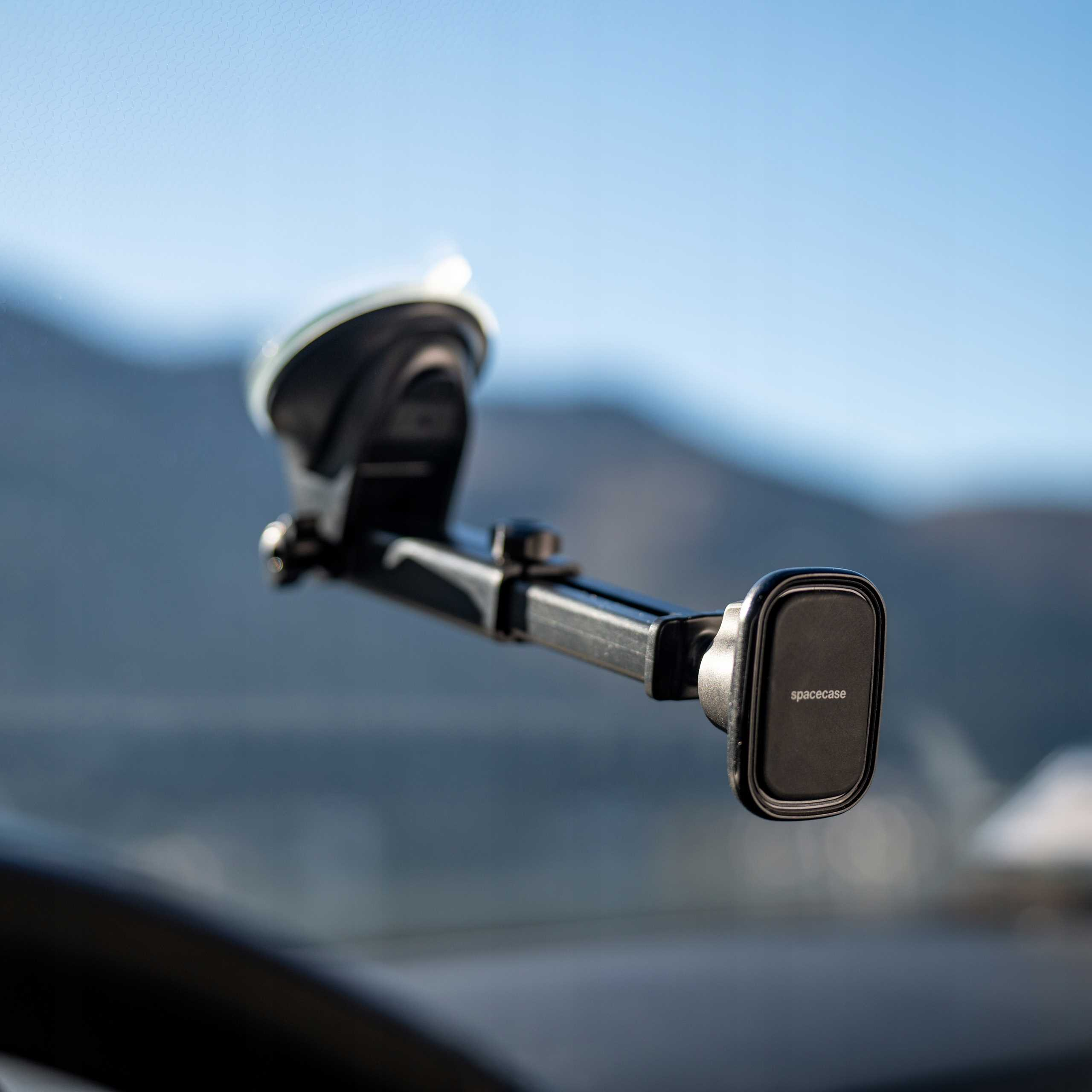 Czarny uchwyt na telefon samochodowy z marką 'spacecase' jest zamontowany na szkle, na tle rozmytego górskiego tła.