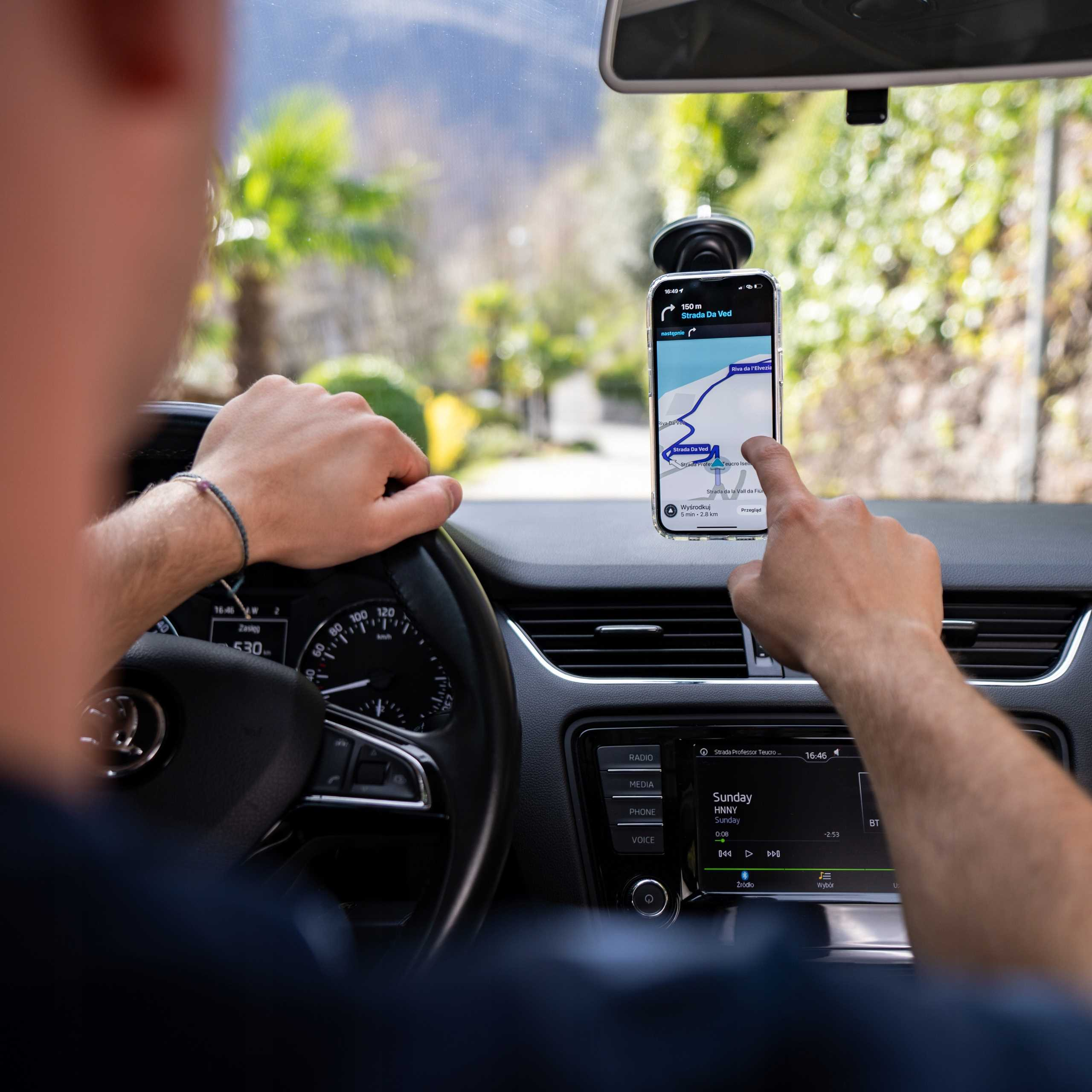 Osoba korzystająca z telefonu z nawigacją w samochodzie. Droga widoczna przez przednią szybę.