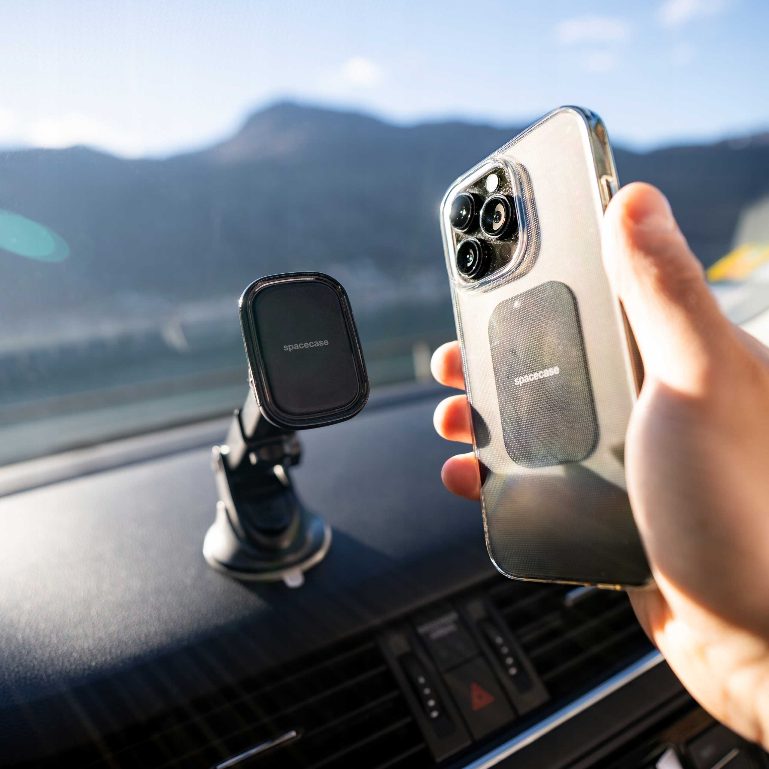 Telefon z naklejką Spacecase trzymany jest blisko uchwytu samochodowego na tle gór.