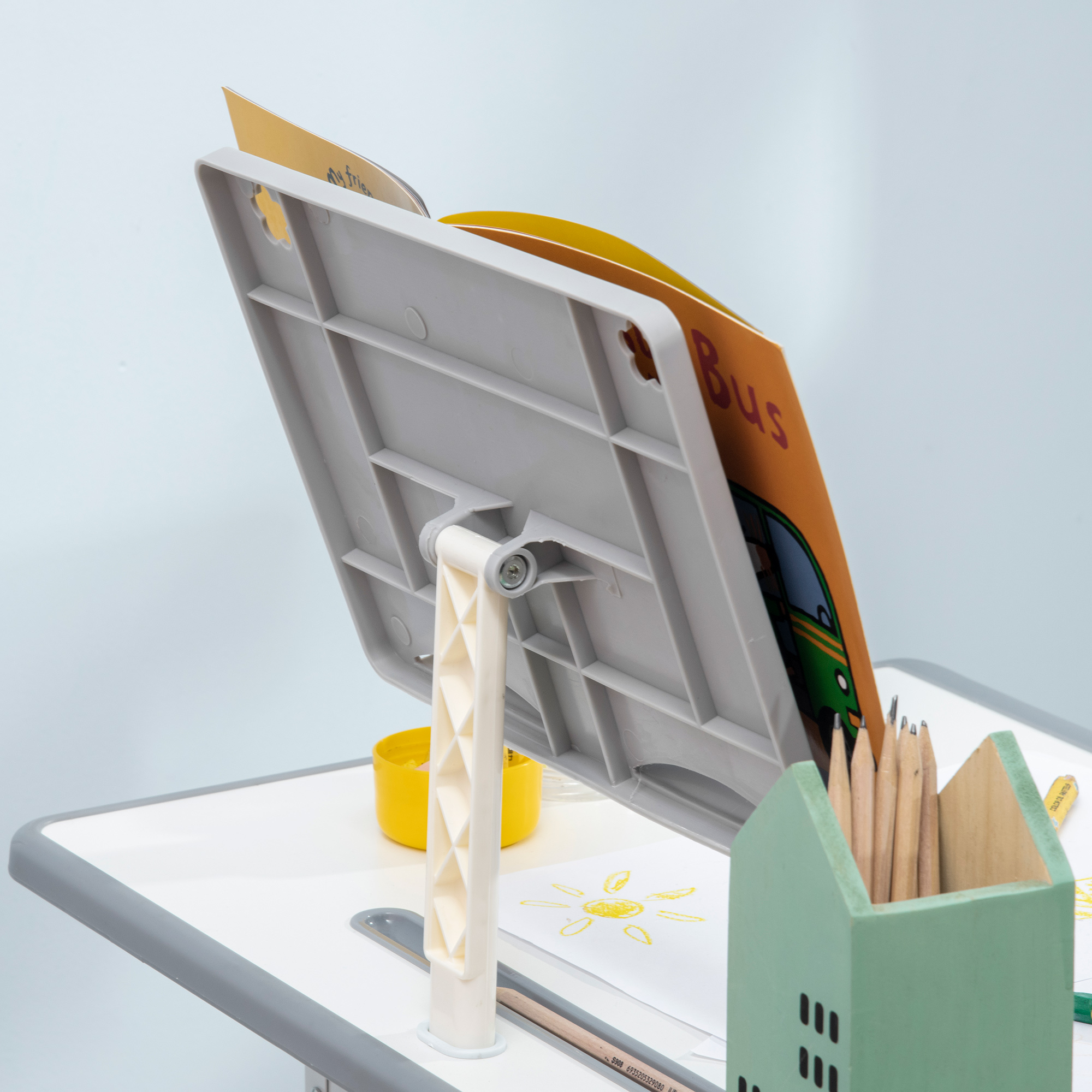 Un libro intitolato 'Bus' è appoggiato su una scrivania. Sono visibili matite e un portamatite verde a forma di casa. Accanto c'è una tazza gialla.