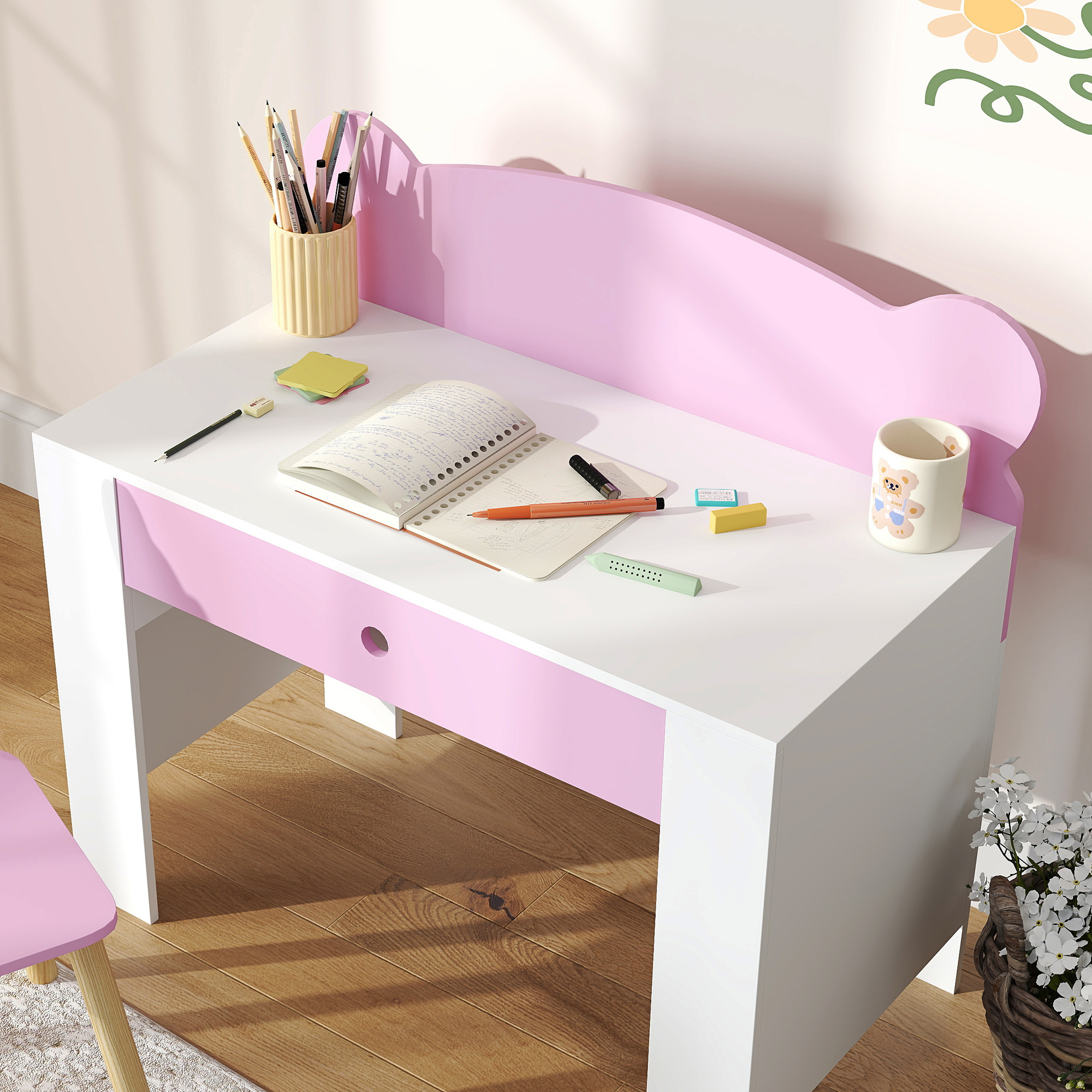 Una scrivania bianca e rosa con cancelleria. Un taccuino, penne e una tazza a forma di orso sono sulla scrivania. Una sedia a sinistra.