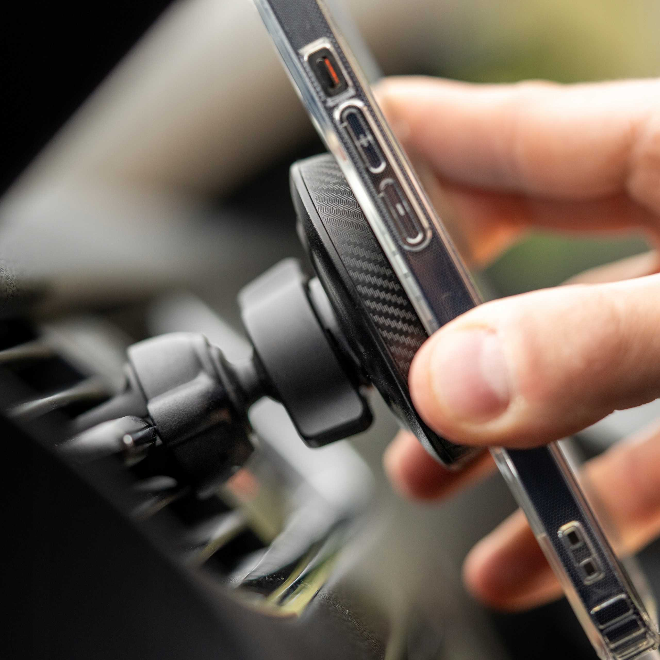 Ręka trzymająca telefon do uchwytu samochodowego. Uchwyt jest czarny, a telefon ma przezroczyste etui.