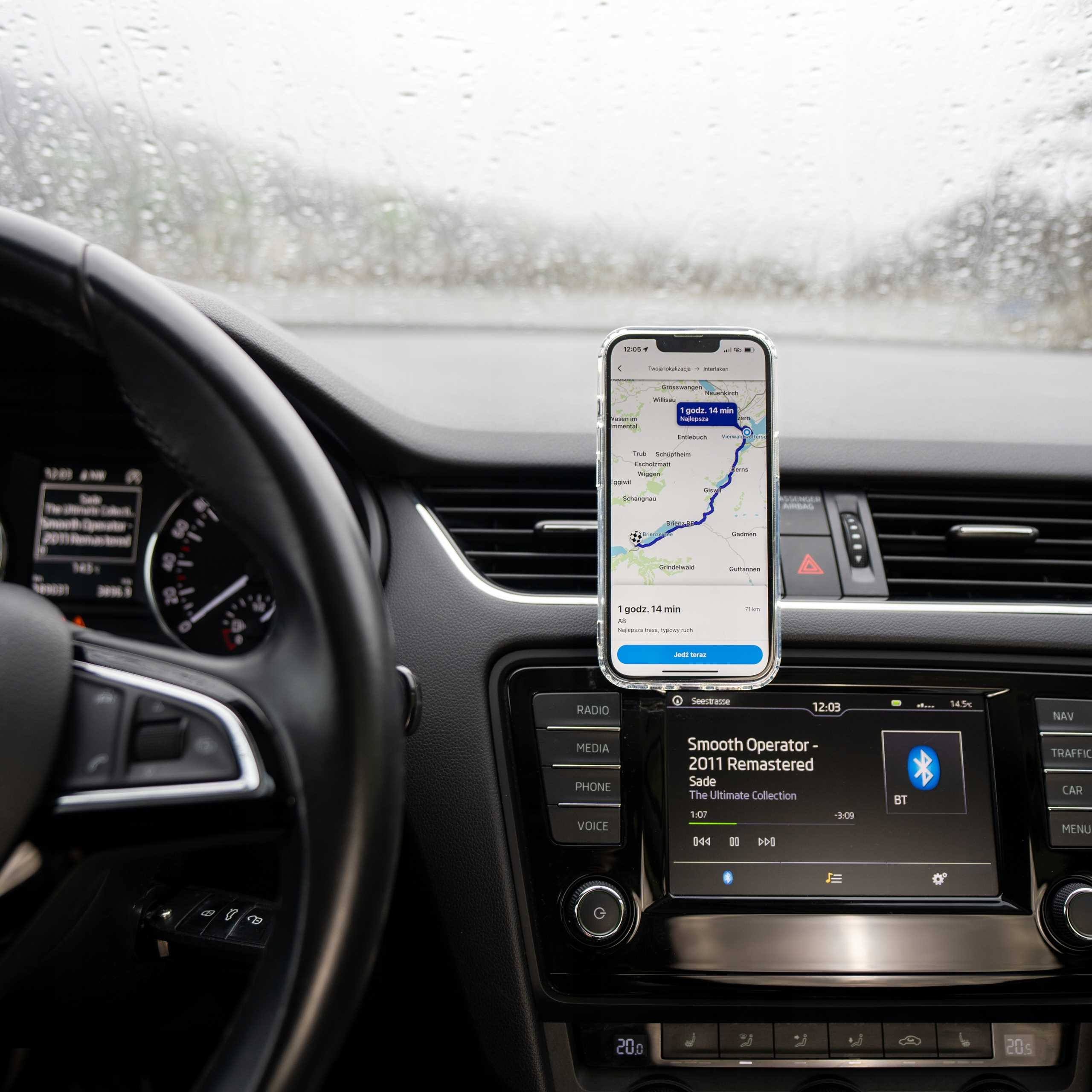 Wnętrze samochodu z telefonem pokazującym nawigację. Kierownica z przodu, deska rozdzielcza z ekranem i przyciskami.