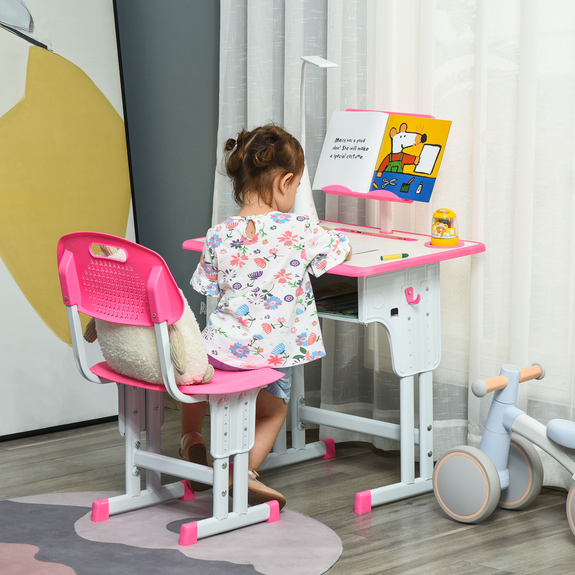 Una bambina è seduta a una scrivania rosa, leggendo un libro. Una pecora di peluche è sulla sedia rosa. Una lampada è vicina.