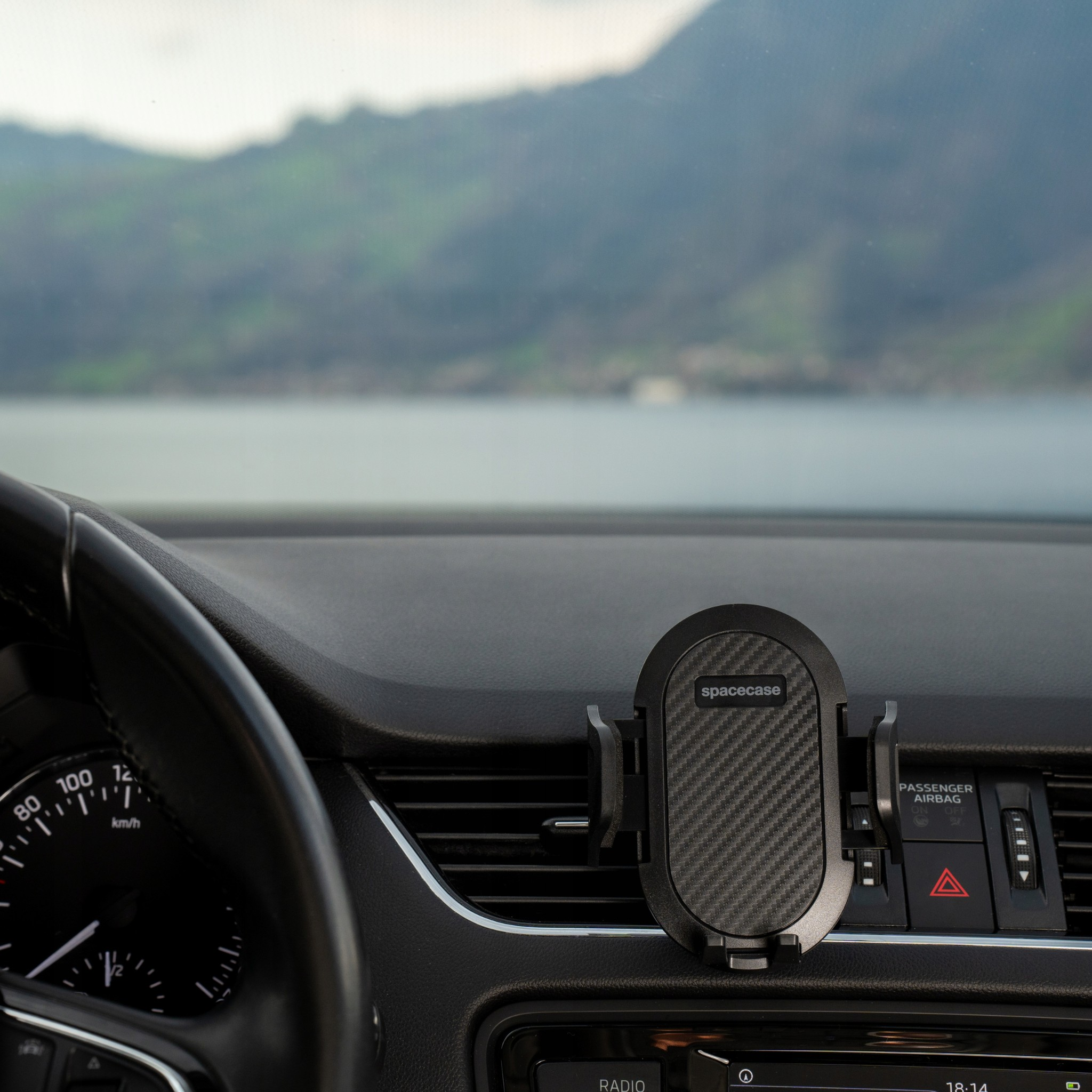 Wnętrze samochodu z uchwytem na telefon. Deska rozdzielcza, kierownica i krajobraz górski w tle.