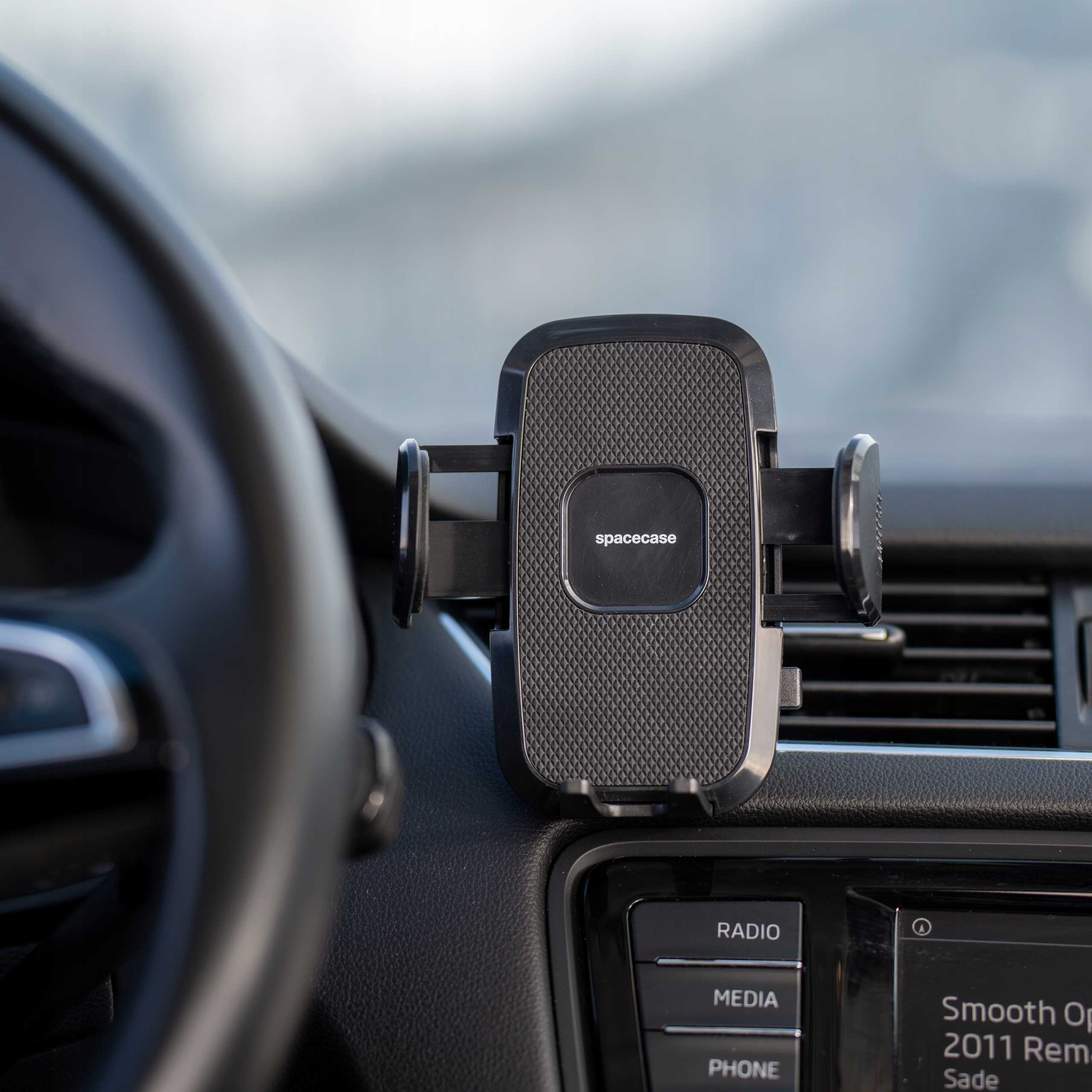 Czarny uchwyt na telefon z napisem 'spacecase' jest zamontowany na desce rozdzielczej samochodu. Kierownica jest po lewej.