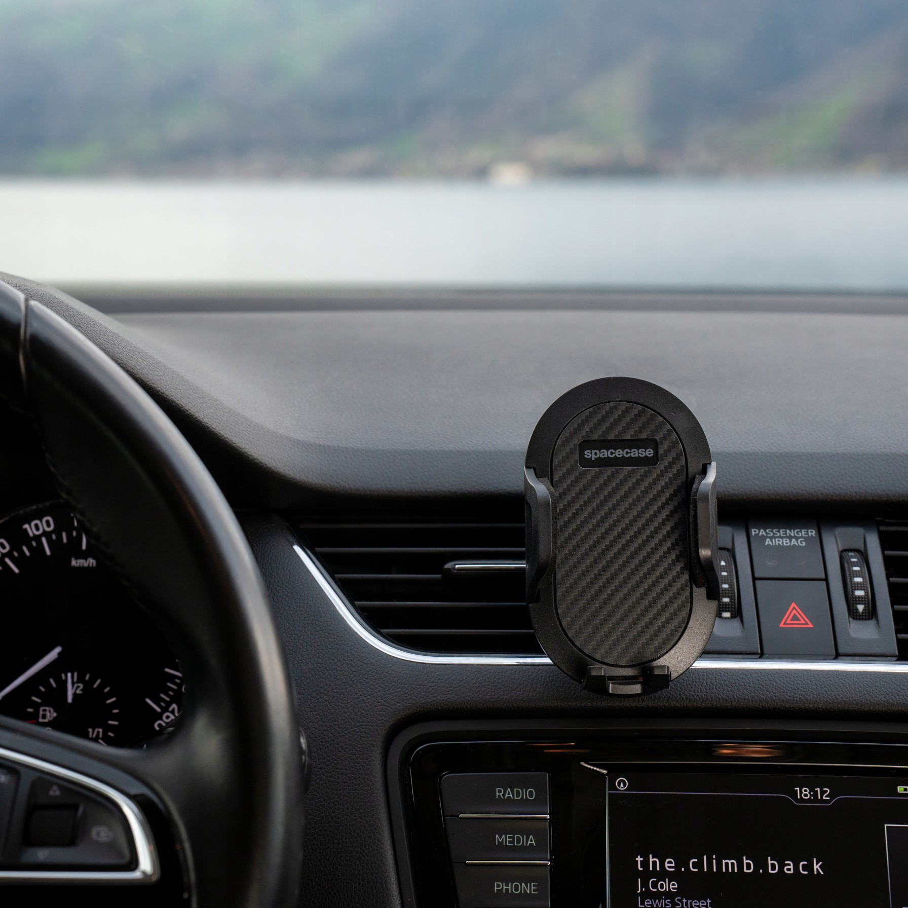 Widok wnętrza samochodu. Uchwyt na telefon na desce rozdzielczej. Widoczna kierownica i jezioro.