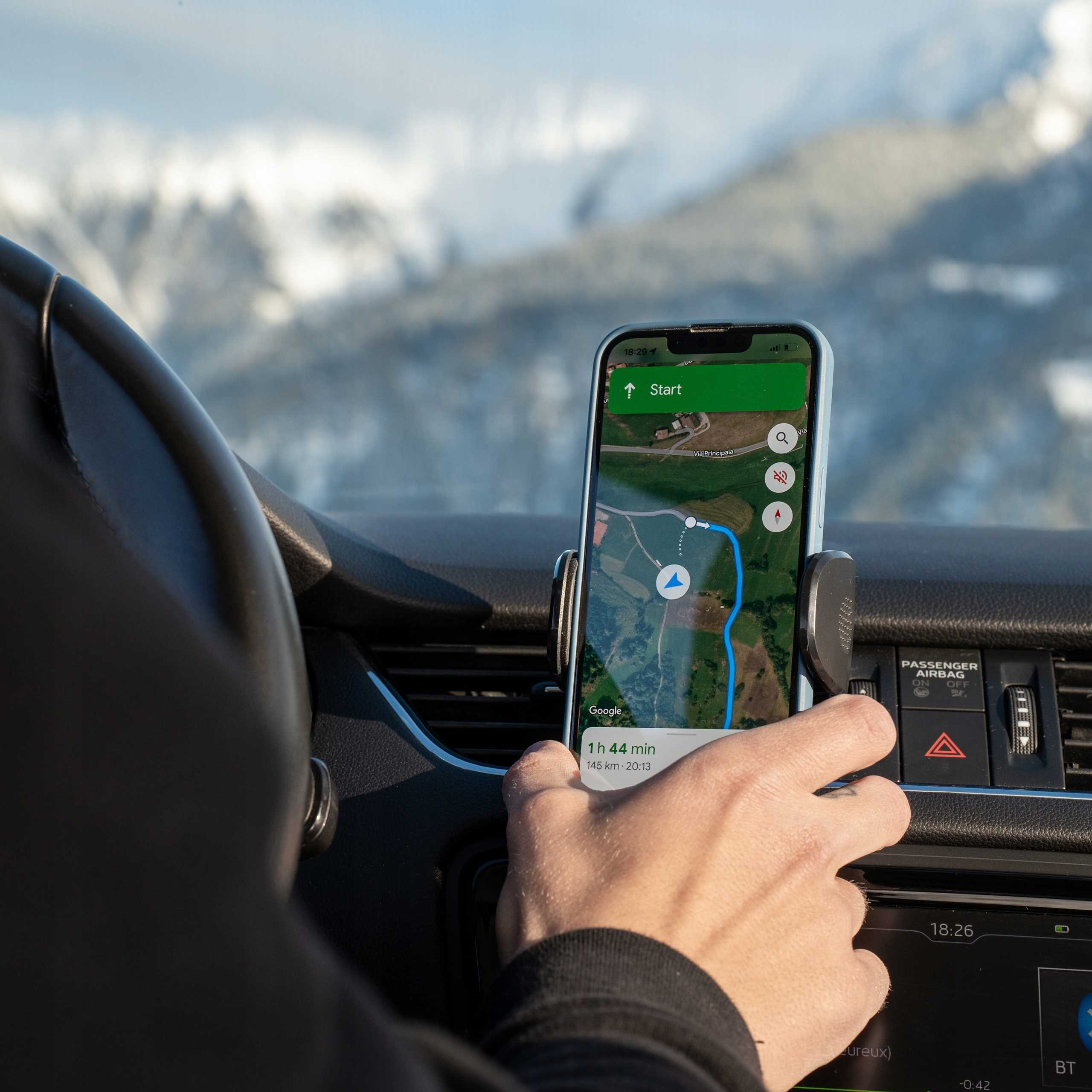 Ręka trzyma telefon z mapą w samochodzie. Przez przednią szybę widać ośnieżone góry.