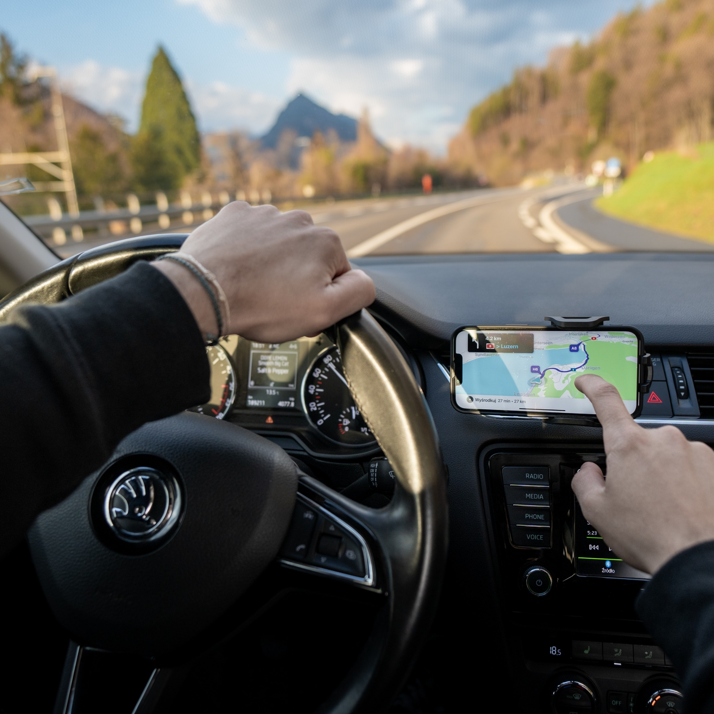 Ręce na kierownicy, telefon z GPS-em. W tle góry i droga.