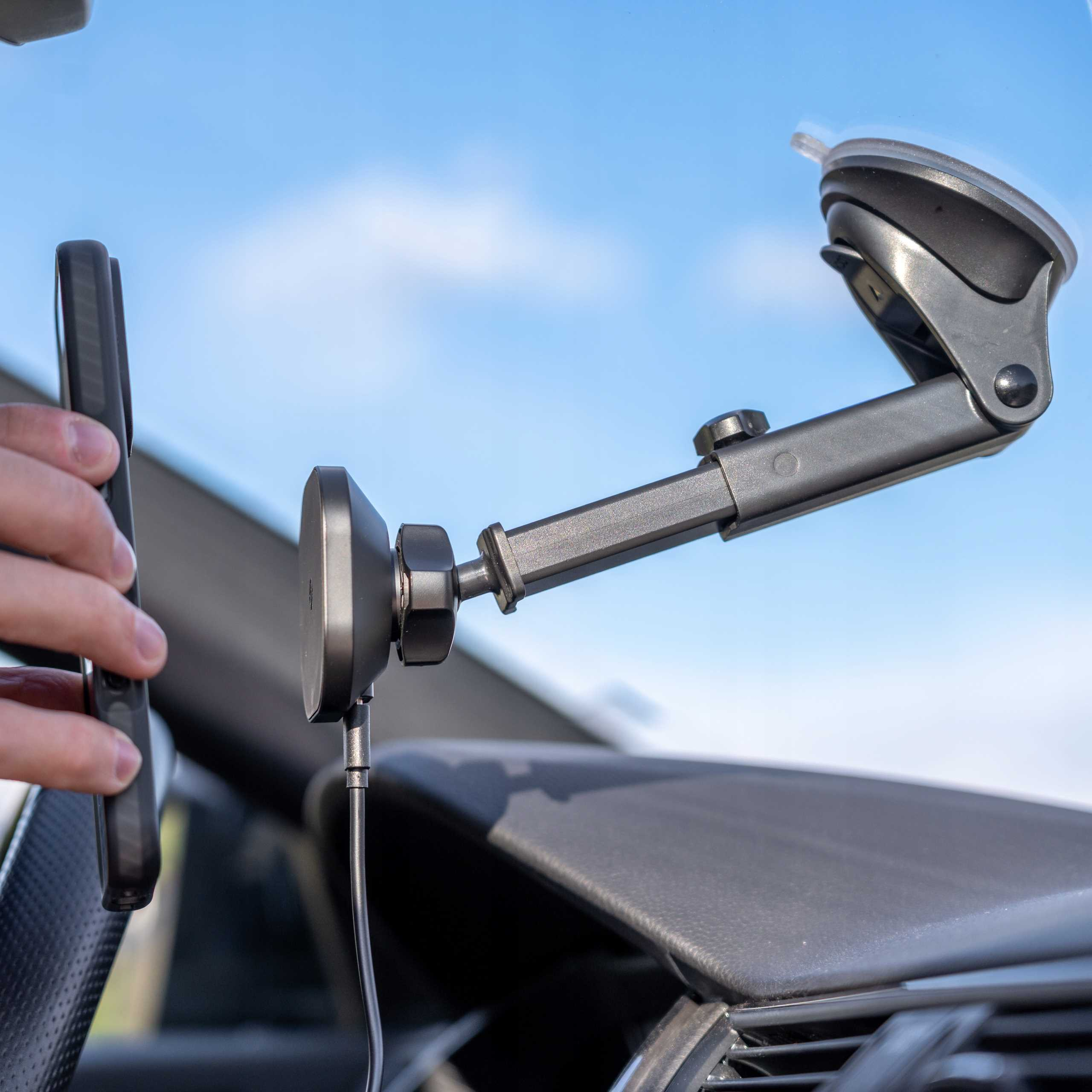 Uchwyt samochodowy na telefon z telefonem. Uchwyt jest zamontowany na przedniej szybie. Ręka trzyma telefon.