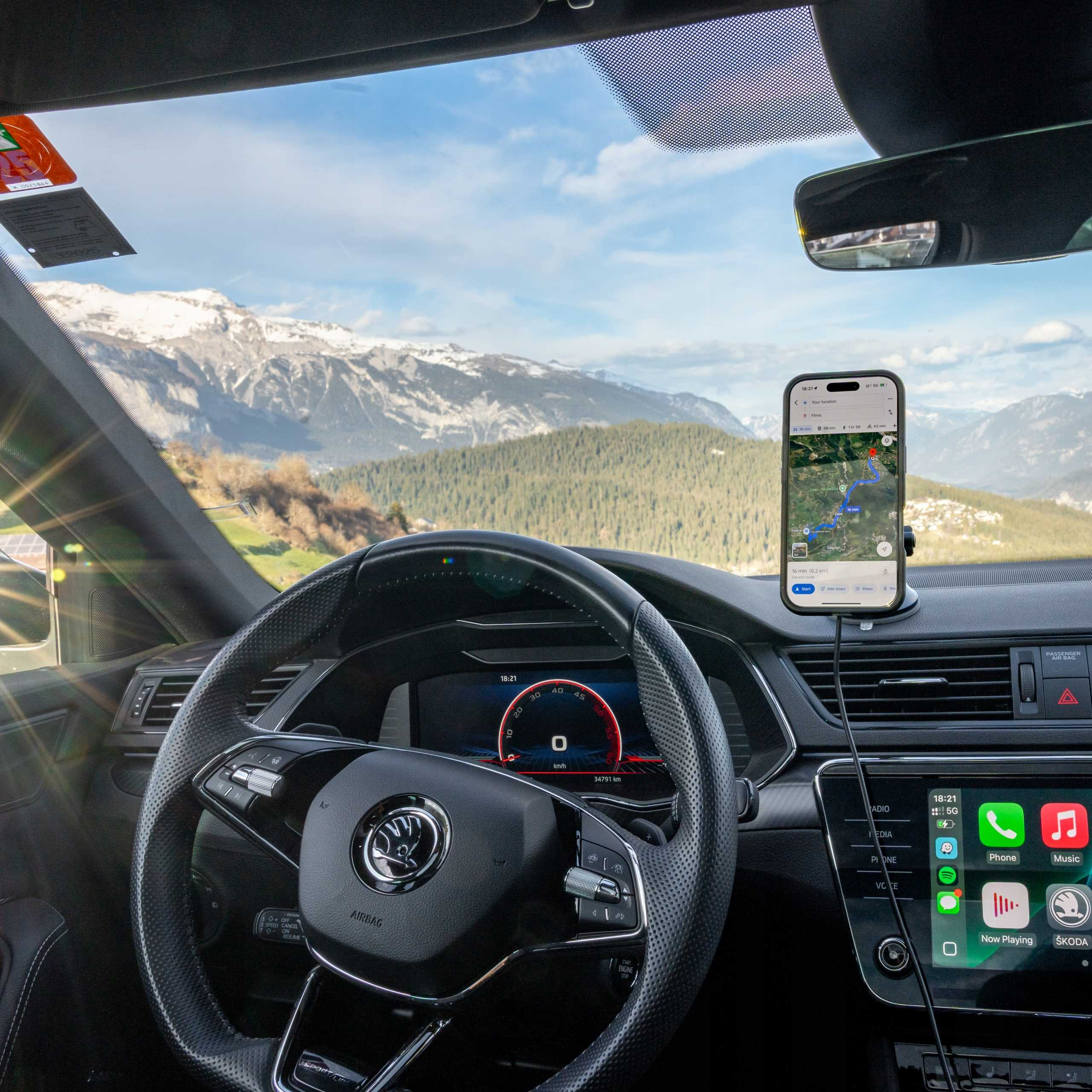 Widok wnętrza samochodu ze smartfonem wyświetlającym aplikację map. Góry widoczne przez przednią szybę. Kierownica na pierwszym planie.